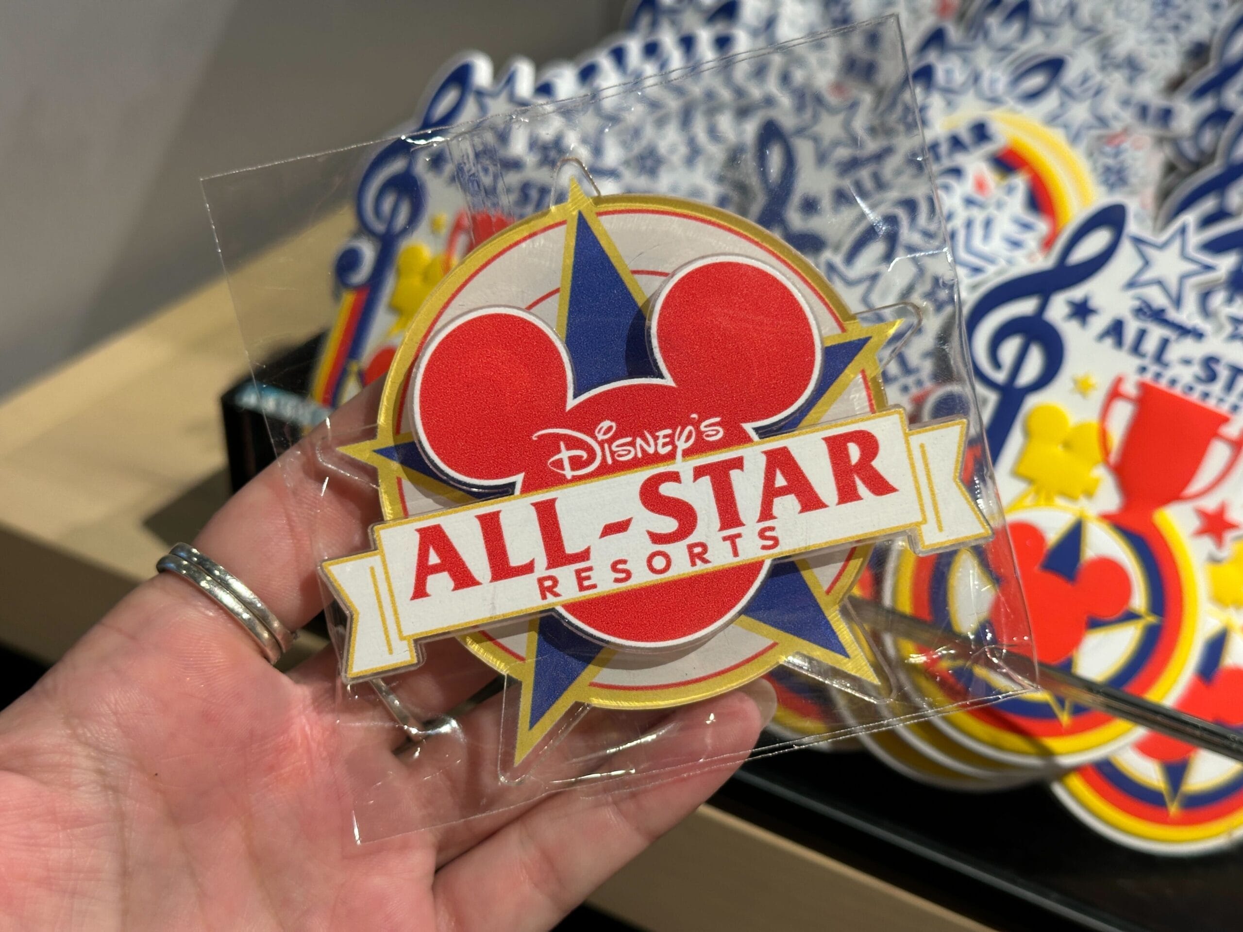 Hand holding a Disney World All-Star Resorts magnet featuring a bold red Mickey head and blue star in the background.