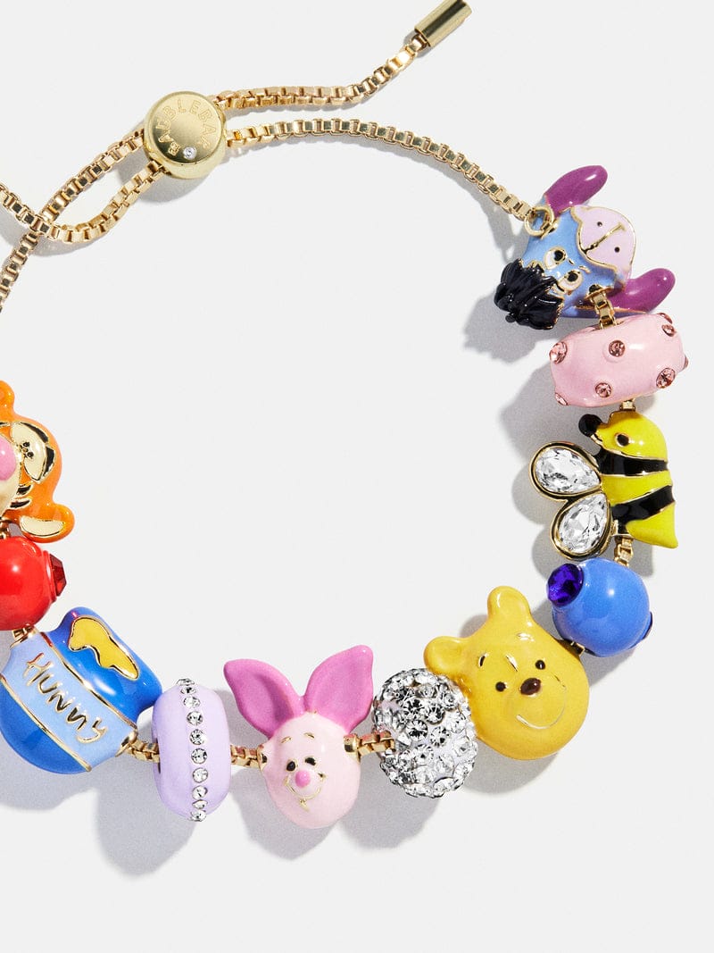 A gold bracelet with colorful Winnie the Pooh charms—Pooh, Piglet, bee, honey pot—just like those found in Disney park shops.