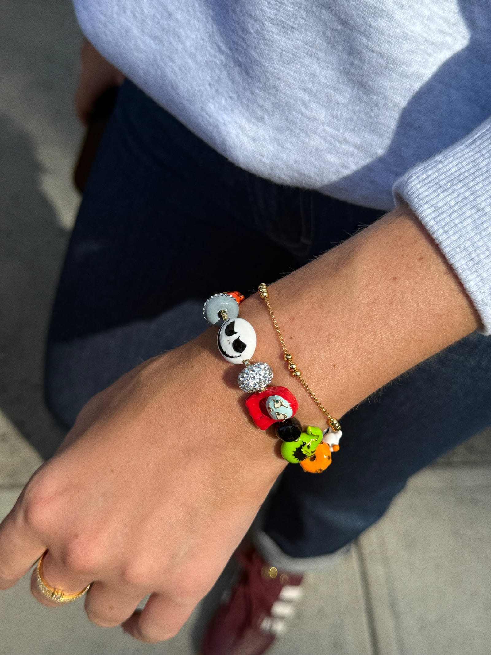 A person at a Disney park shows off colorful beaded Halloween bracelets, wearing jeans and a gray top, no castle in view.