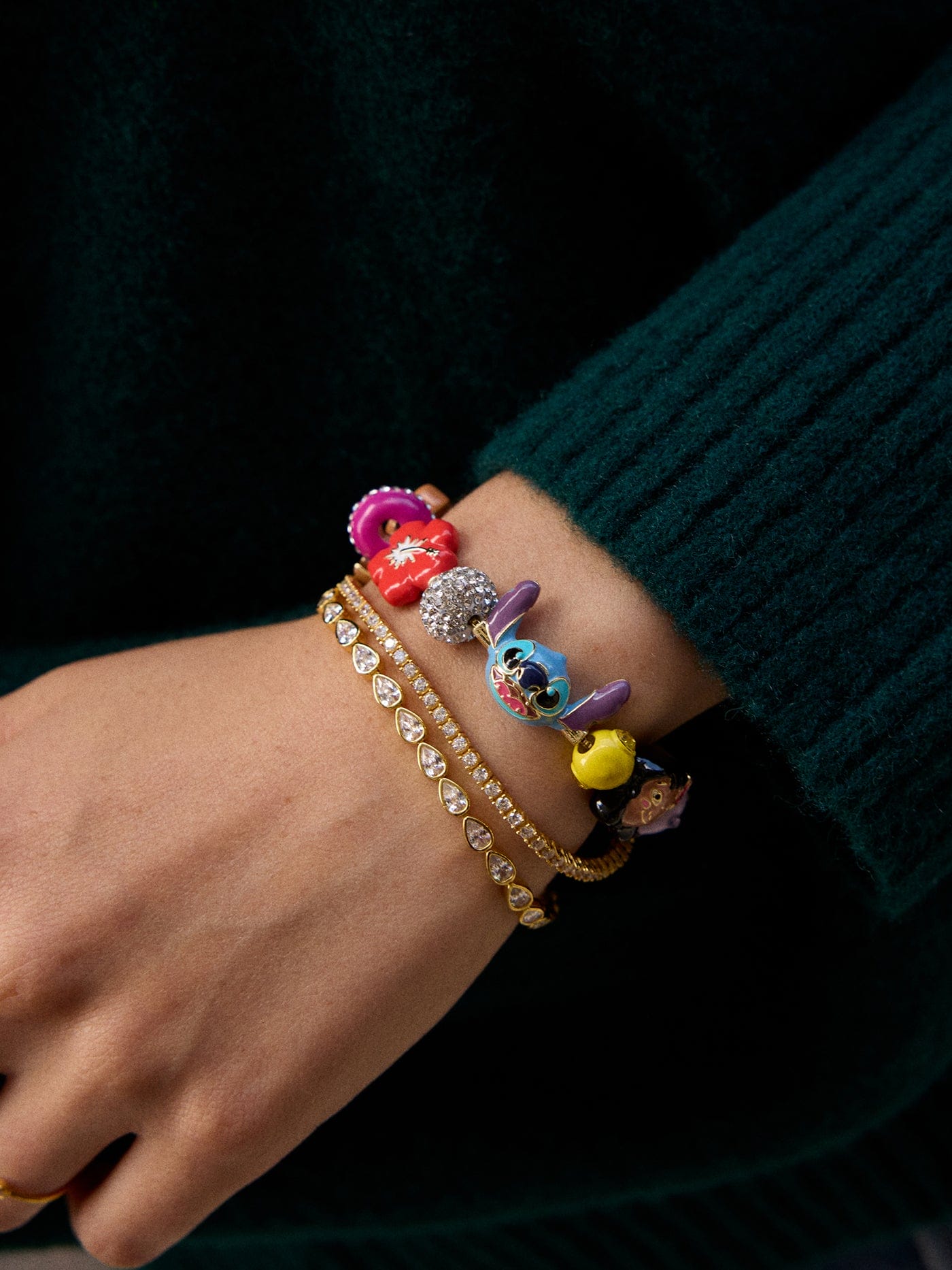 A hand with gold bracelets and a Disney character charm bracelet, reminiscent of souvenirs from Disneyland parks worldwide.