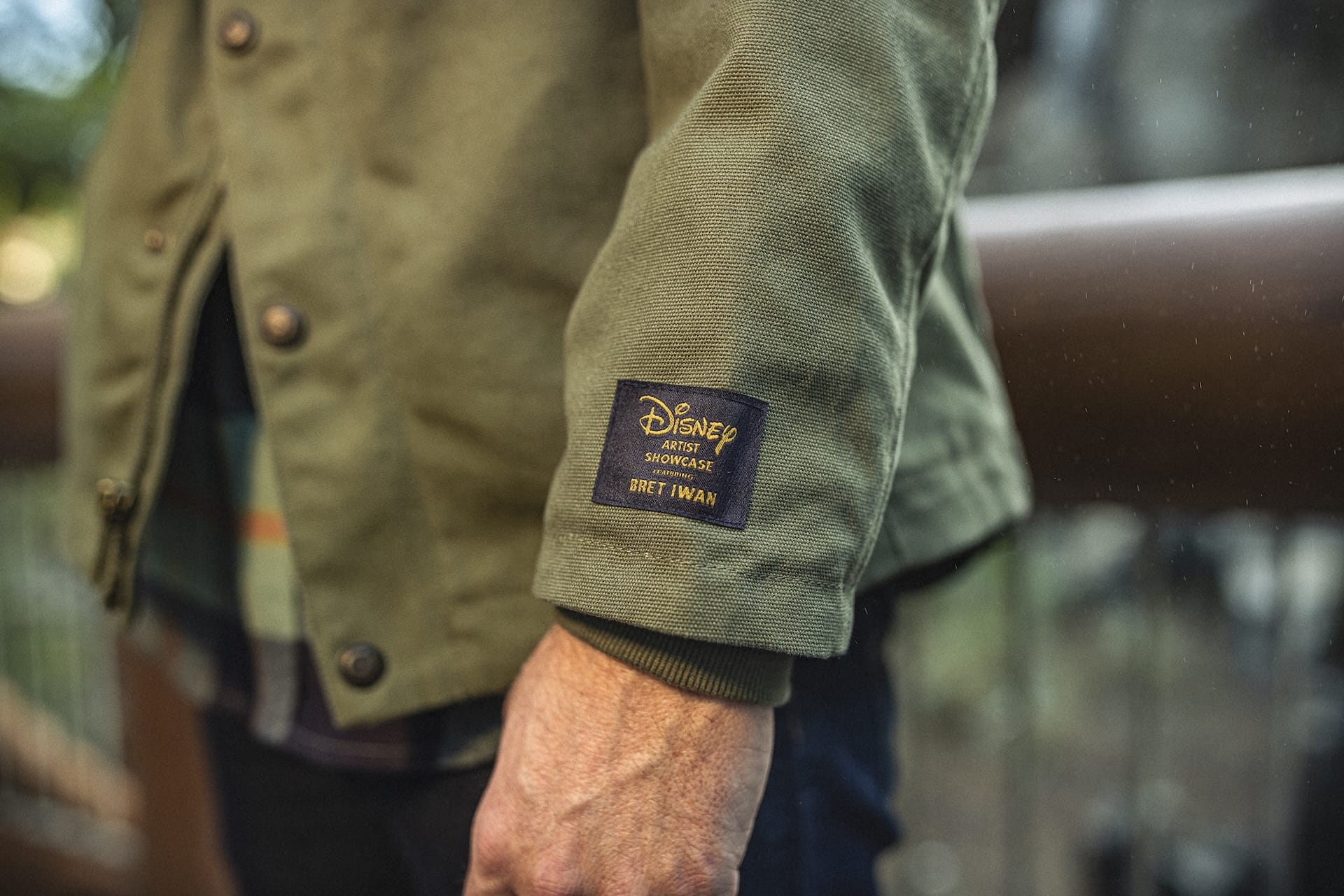 A park guest in a green Expedition Mickey Mouse jacket, featuring a "Disney x Worn Wear" patch on the sleeve.