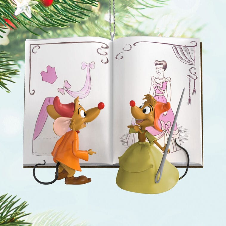 Two mice in clothes stand by a Cinderella storybook and Disney ornaments, evoking park shop displays near Christmas decor.