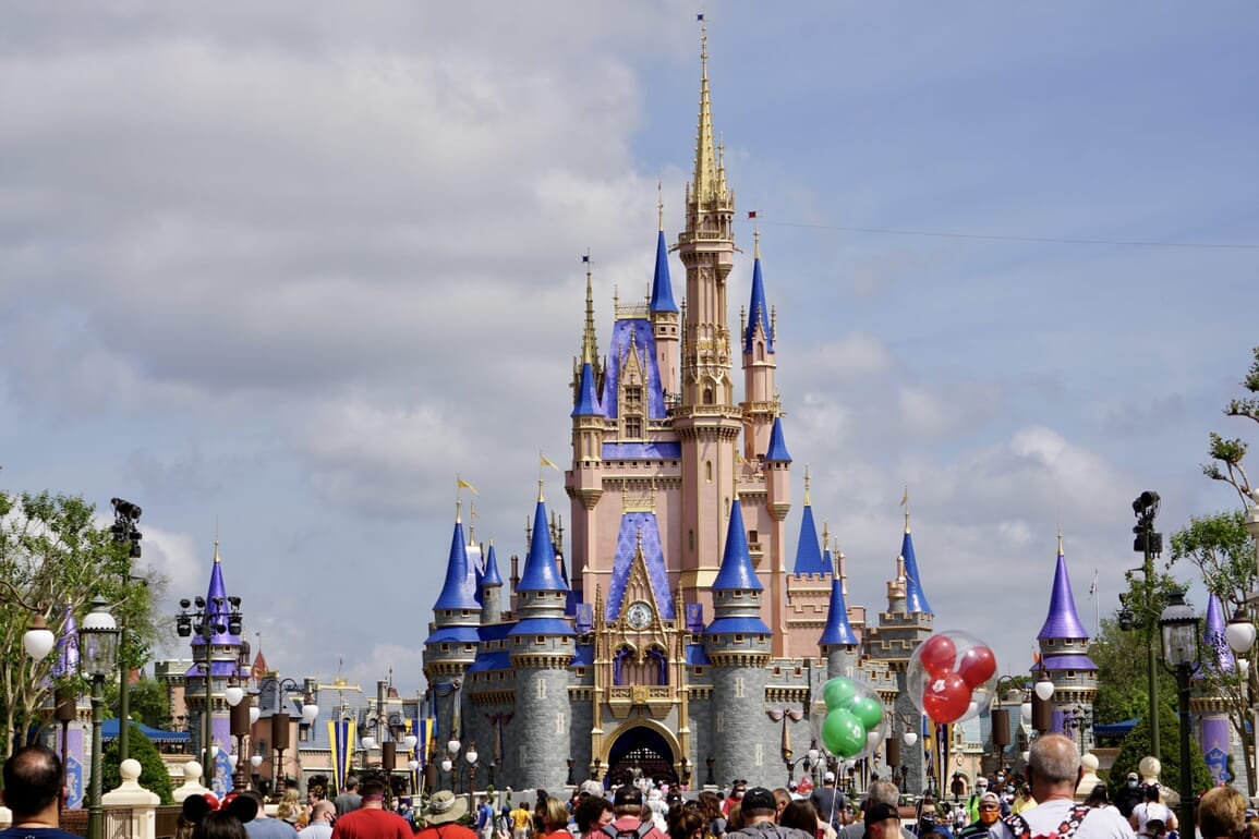 Cinderella Castle at Walt Disney World with crowds and bright balloons.