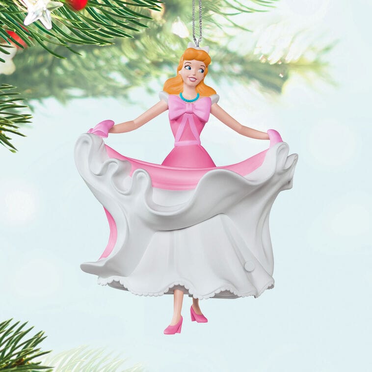 Disney ornament of a joyful woman in a pink dress lifting her white skirt, hanging from a Christmas tree, evoking park elegance.