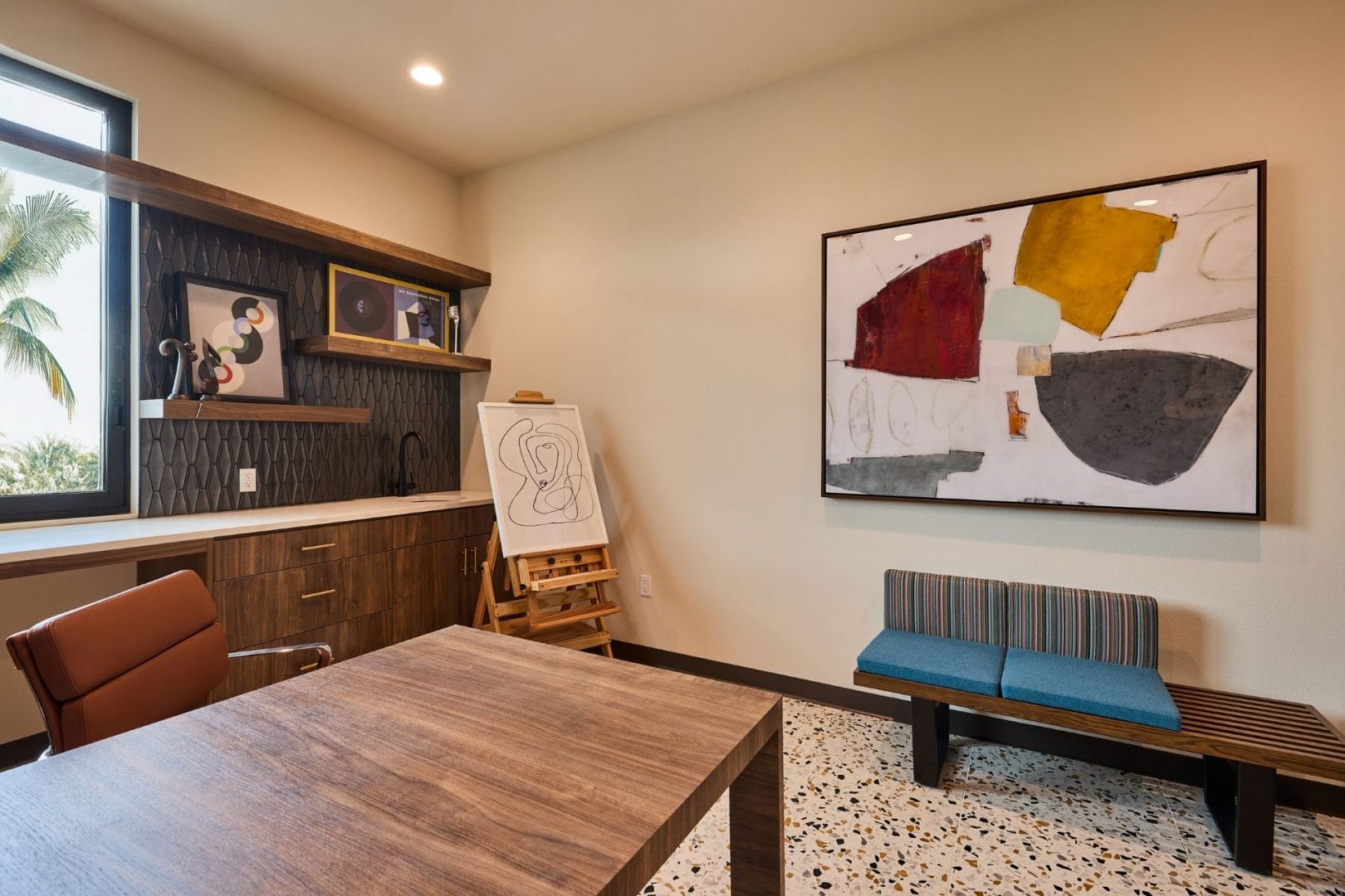 Modern home office styled like Disney Parr House at the parks; wooden desk, abstract art above, small bench beneath the painting.