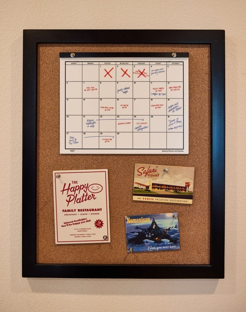 A corkboard with a calendar and three colorful Disney postcards, Parr House–inspired, framed in black—no Disney castle shown.