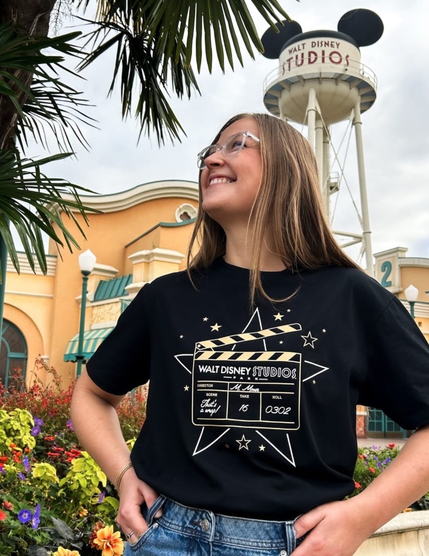 Smiling woman in glasses at Walt Disney Studios Park, wearing a Final Take Farewell Collection Hollywood star shirt—no castle visible.