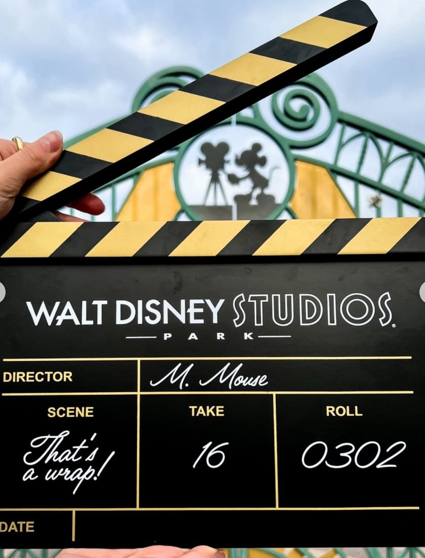 A film clapperboard labeled "Final Take" is held by green gates and the classic Mickey Mouse statue at Walt Disney Studios Park.