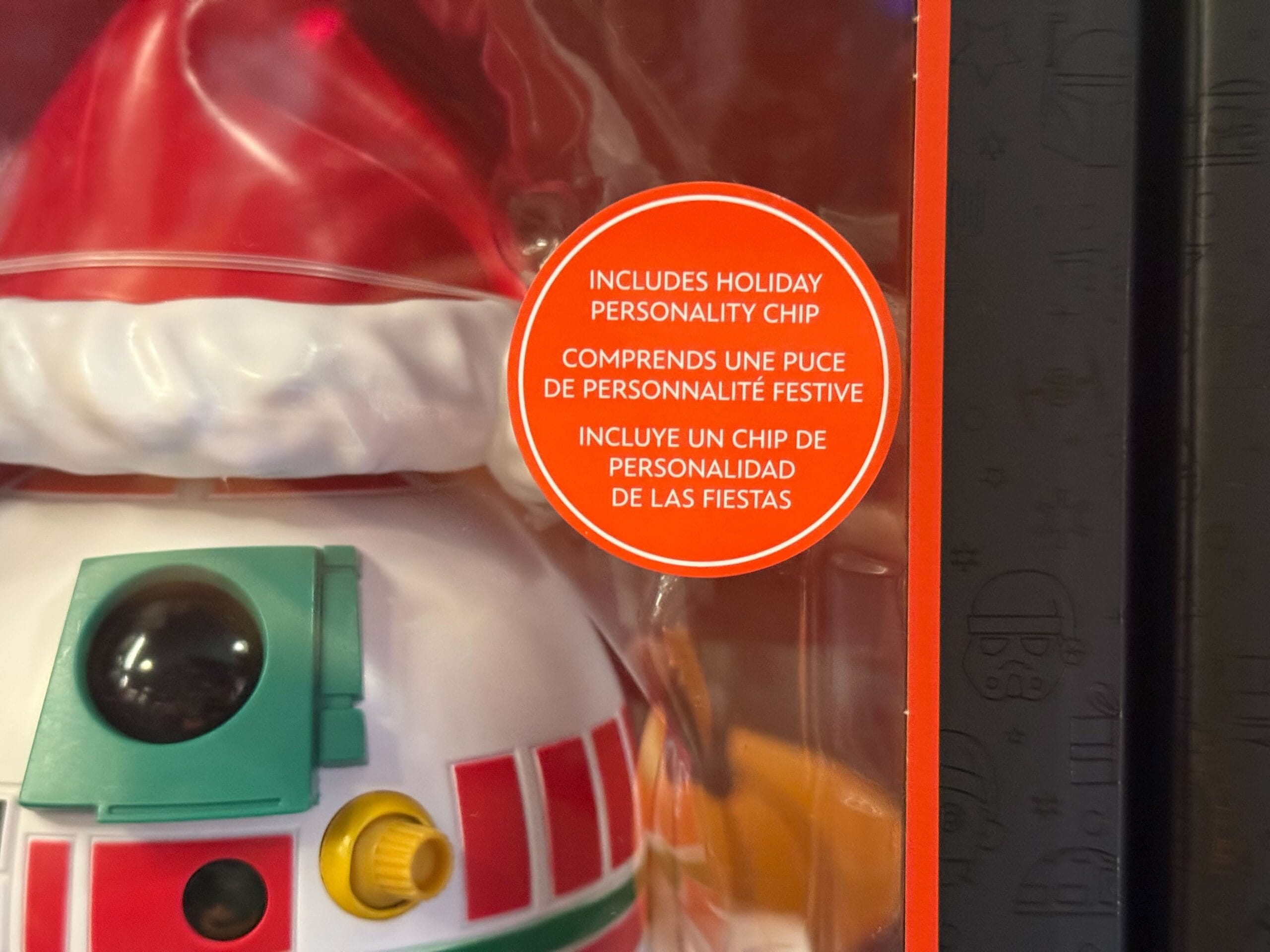 Close-up of 2025 Disneyland Christmas merchandise toy with a label about a holiday personality chip in three languages.