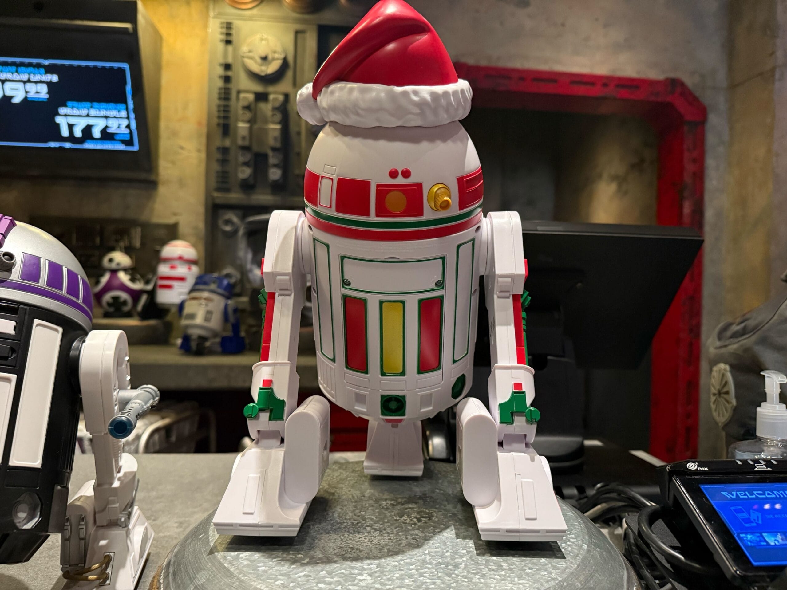 A festive R2-D2-style droid toy in a Santa hat, part of 2025 Disneyland Christmas merchandise, displayed indoors.