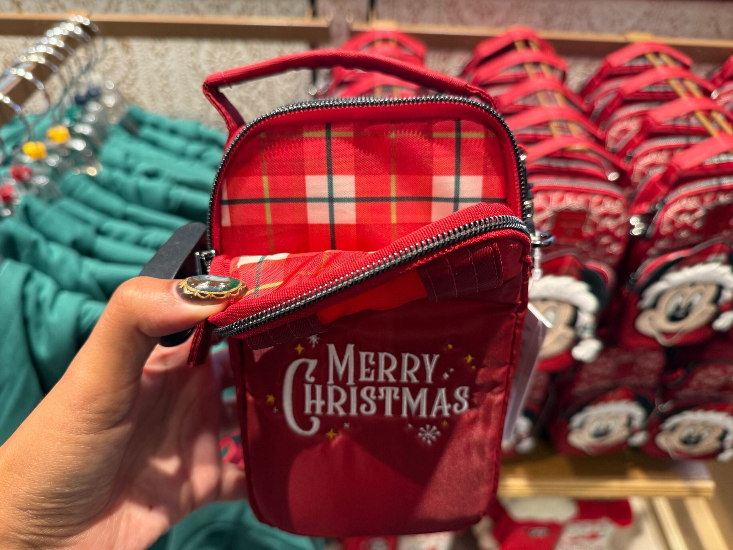 A hand holds an open red pouch with "Merry Christmas" text, part of the 2025 Disneyland Christmas merchandise lineup.