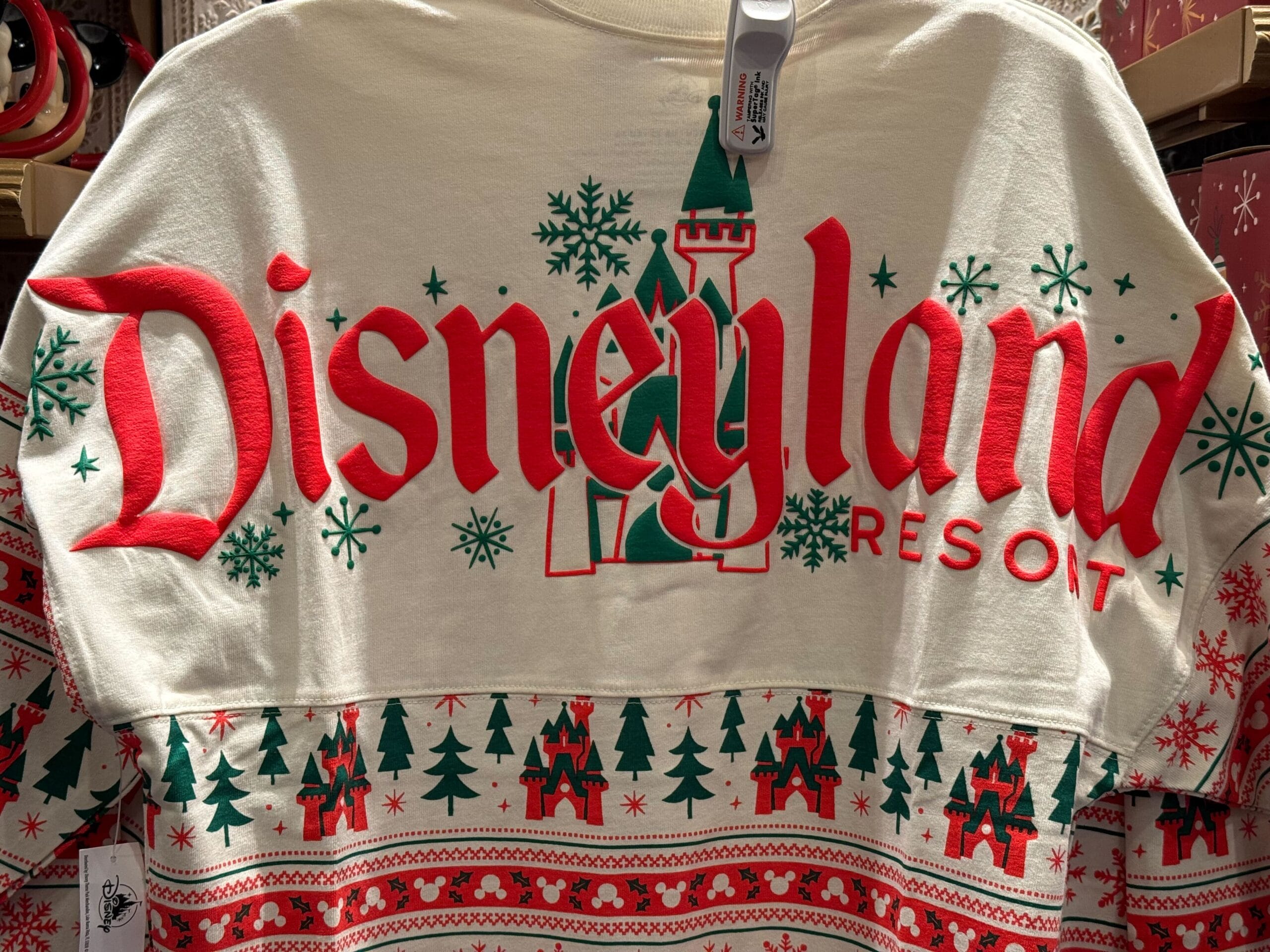 A 2025 Disneyland Christmas merchandise holiday sweater with festive trees, snowflakes, and red and green lettering.