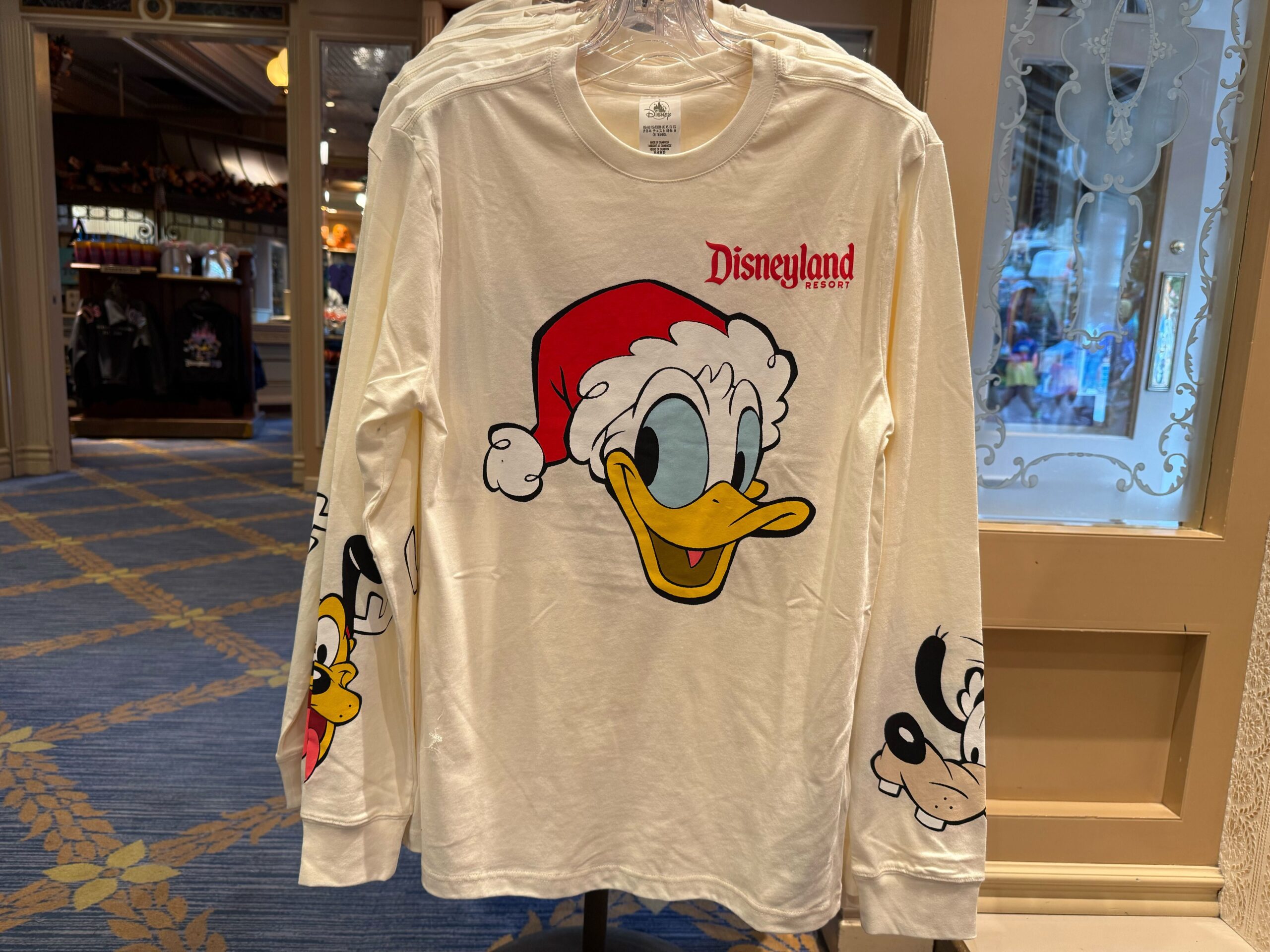 Long-sleeve white Disneyland Christmas merchandise shirt with Donald Duck in a Santa hat, plus Pluto and Goofy on the sleeves.