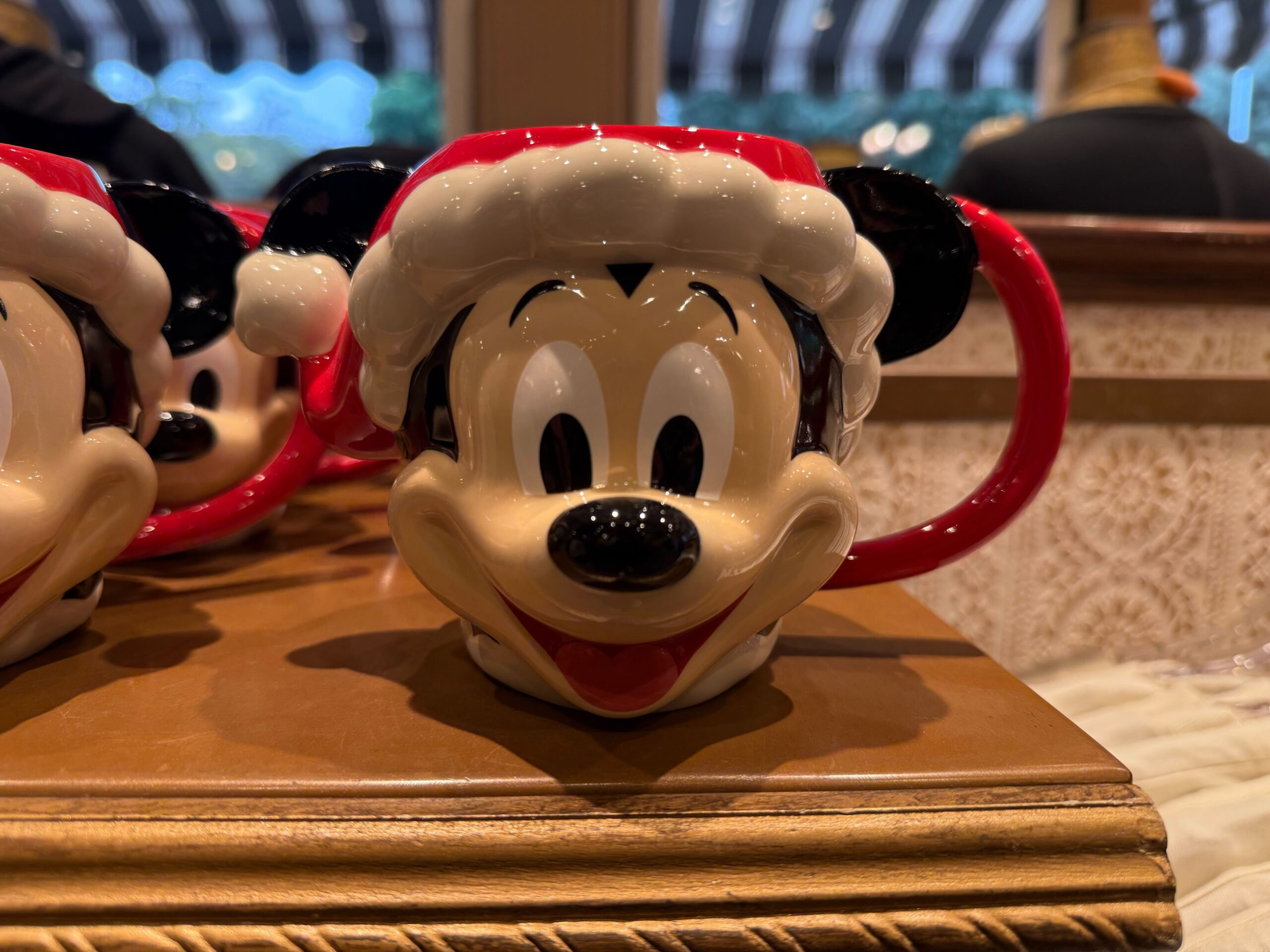 A ceramic mug shaped like Mickey Mouse in a Santa hat, part of 2025 Disneyland Christmas merchandise, sits indoors.