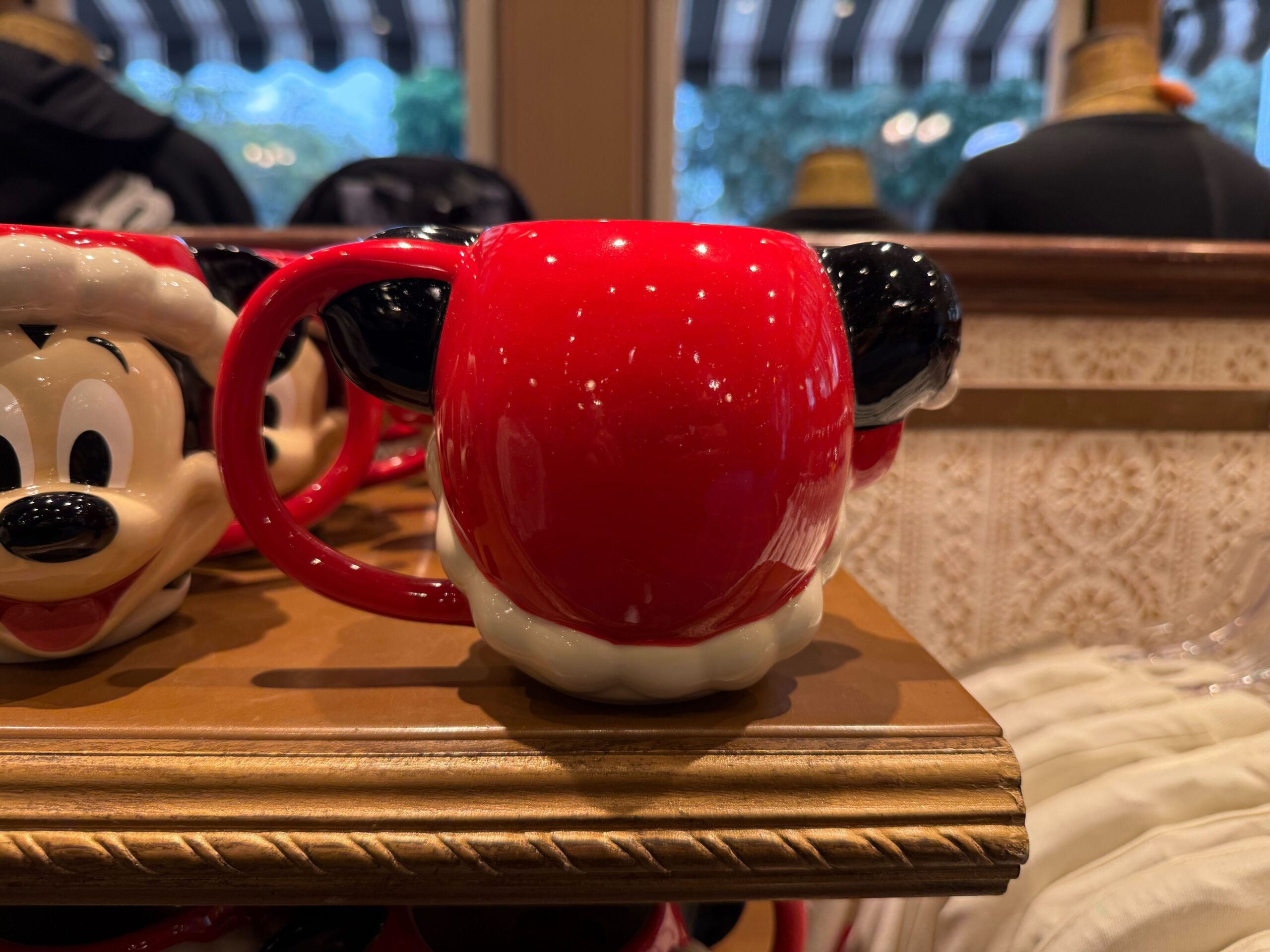 A red mug shaped like Mickey Mouse's head with a Santa hat, part of Disneyland Christmas Merchandise, on a store shelf.