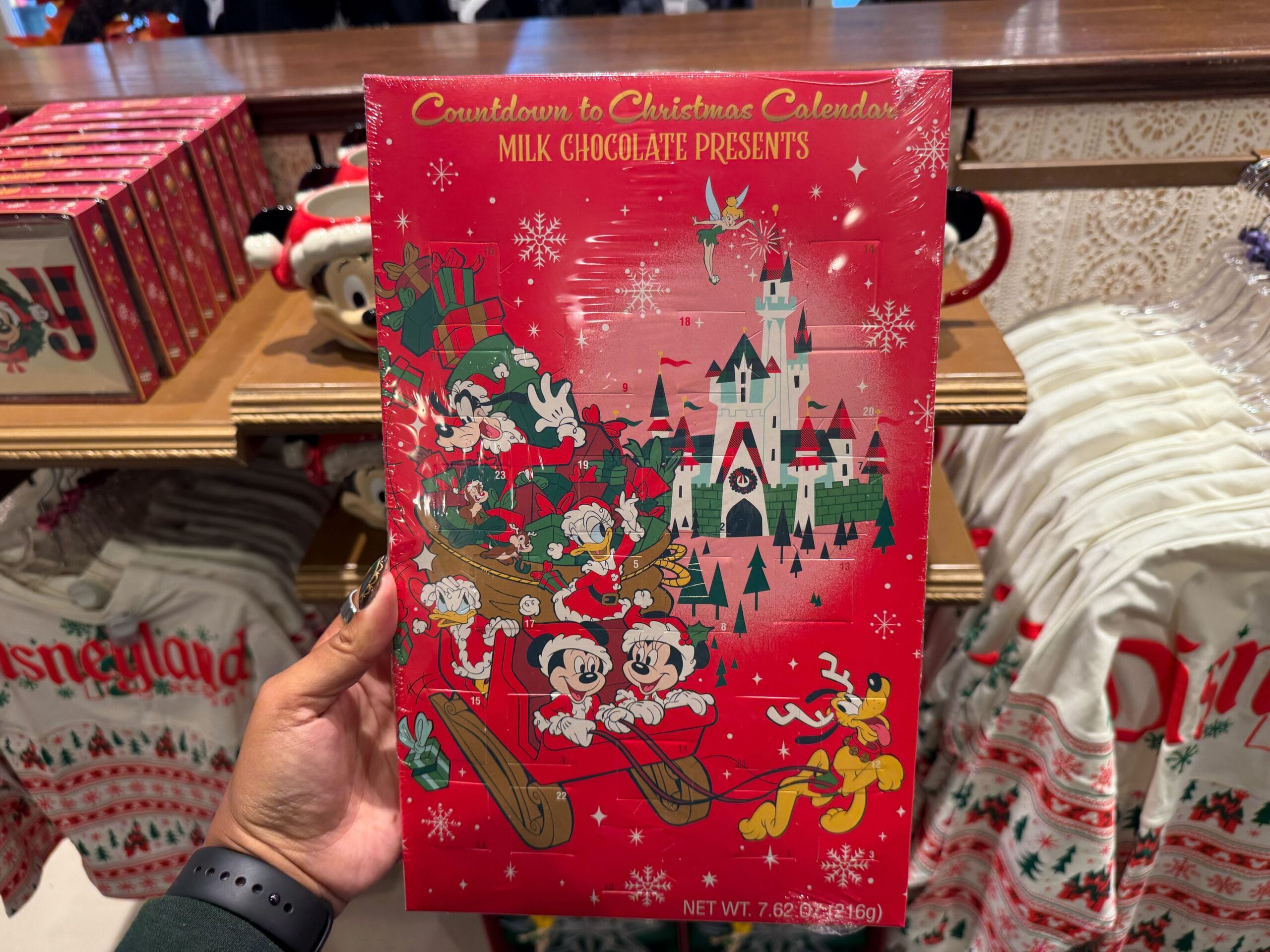 Hand holding a red Christmas chocolate calendar—Disneyland Christmas merchandise featuring Mickey and friends in festive attire.