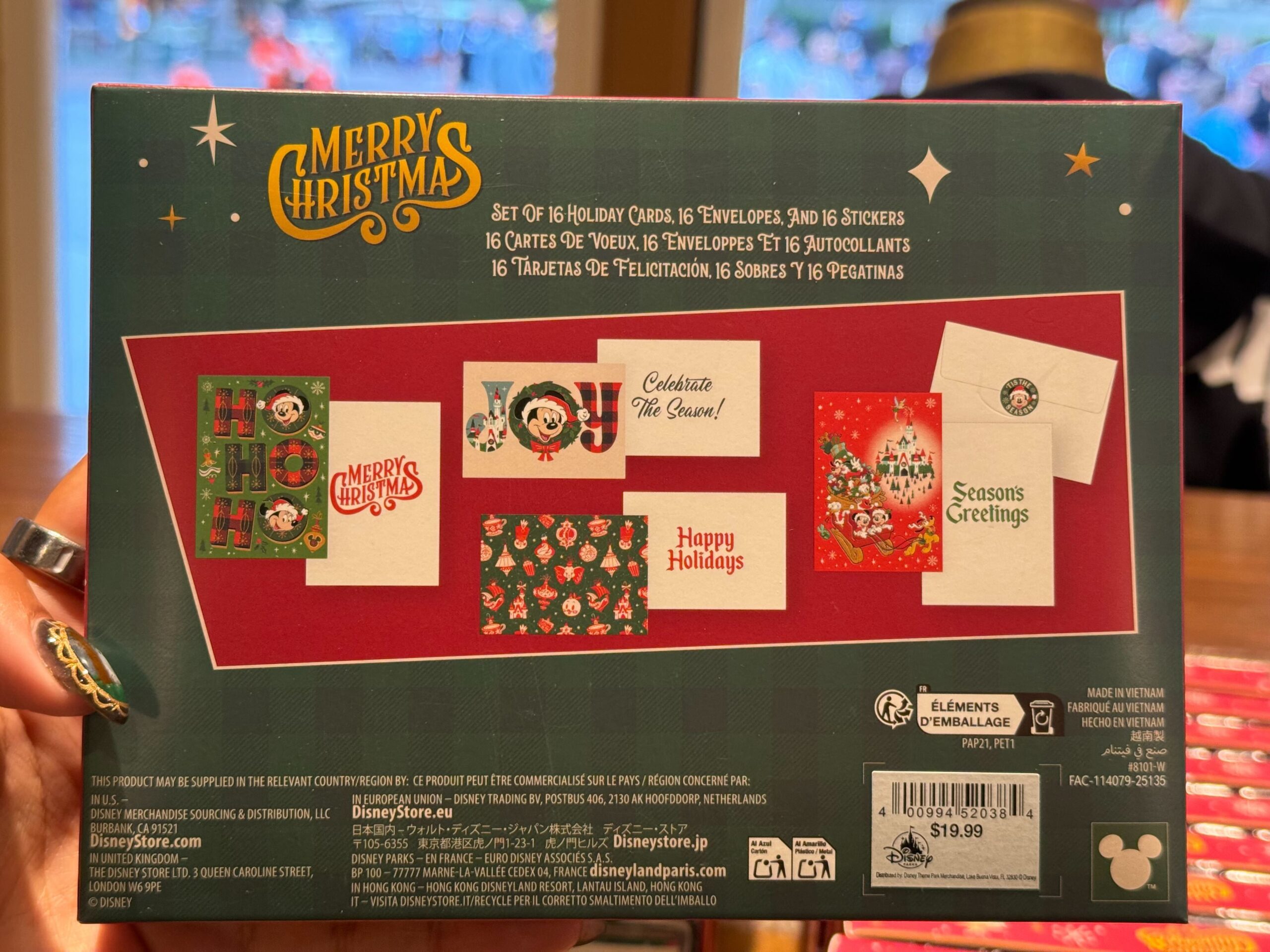 Back of a 2025 Disneyland Christmas merchandise card box showing six designs, prices, and a hand holding it in-store.