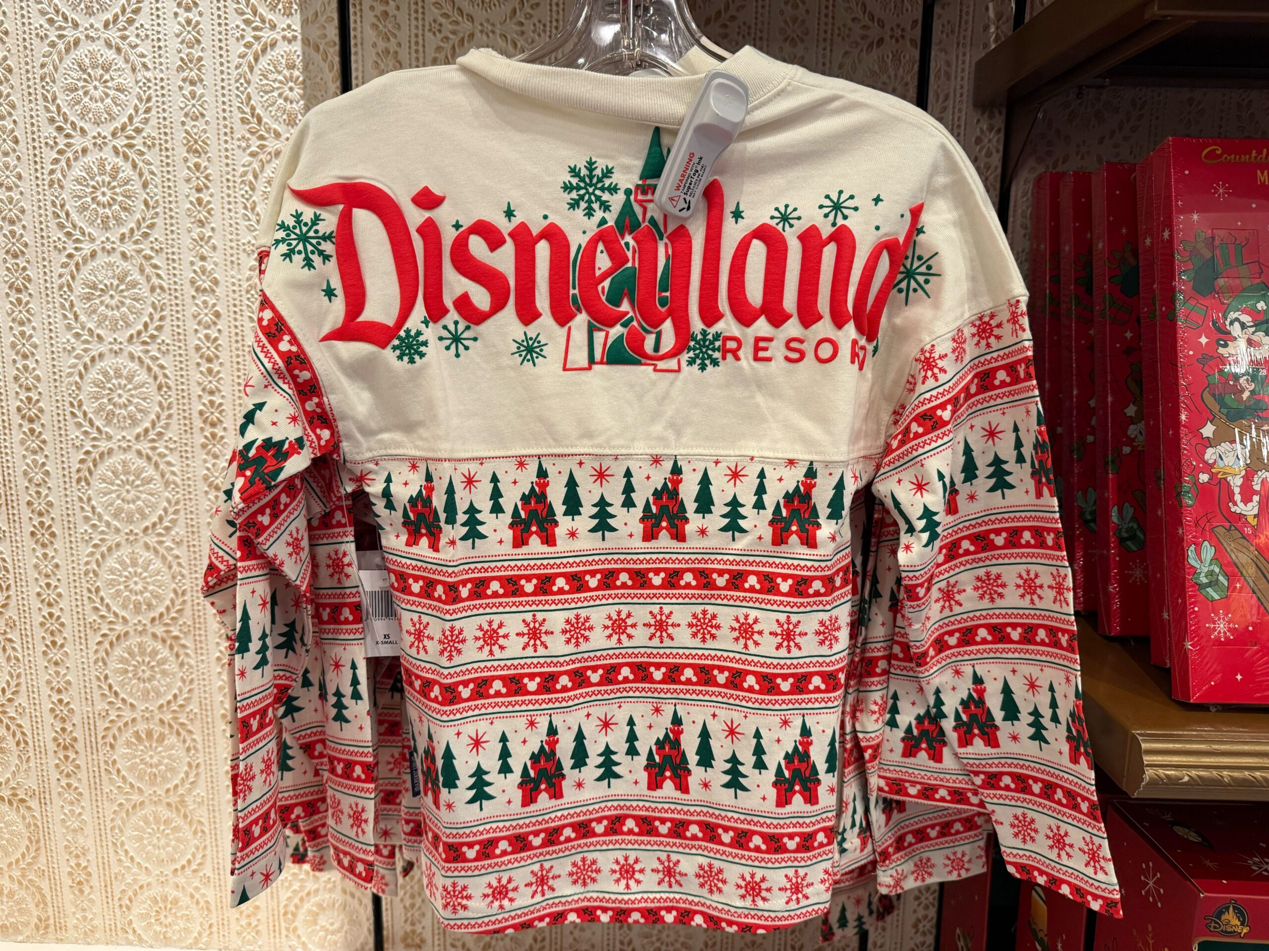 A Disneyland Christmas merchandise shirt featuring festive trees, snowflakes, and holiday patterns for 2025 Disneyland celebrations.
