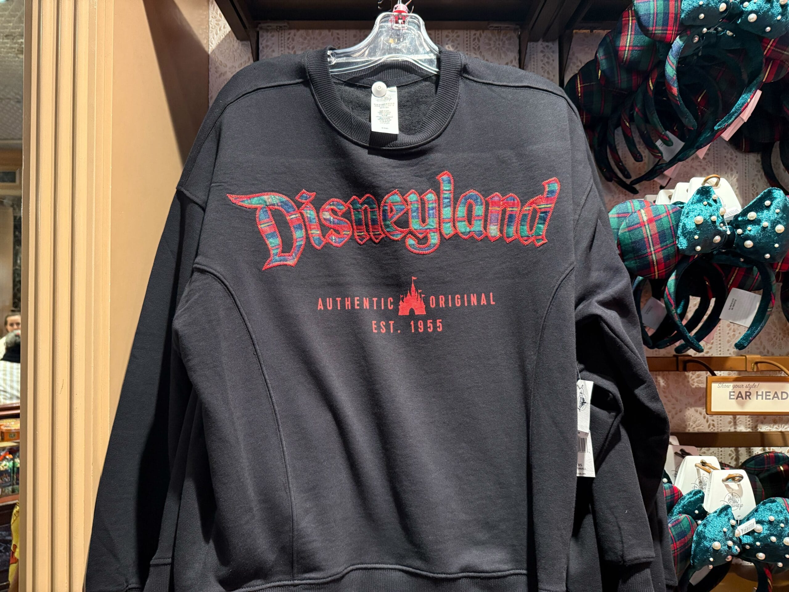 A black sweatshirt from the 2025 Disneyland Christmas merchandise line hangs on a store rack.