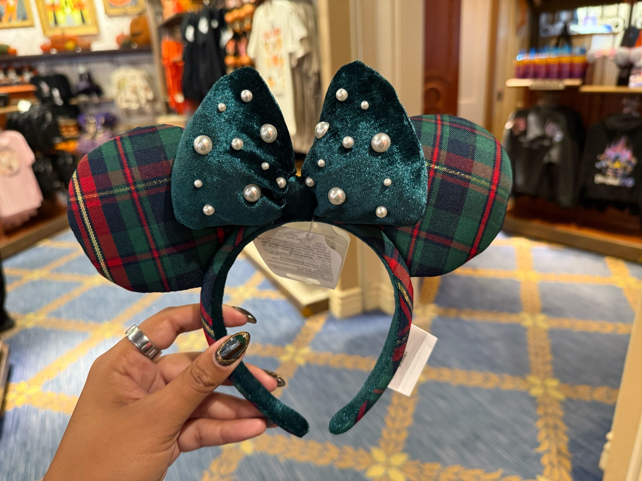 A hand holds a plaid Minnie Mouse ear headband with pearls—a festive 2025 Disneyland Christmas merchandise find in store.