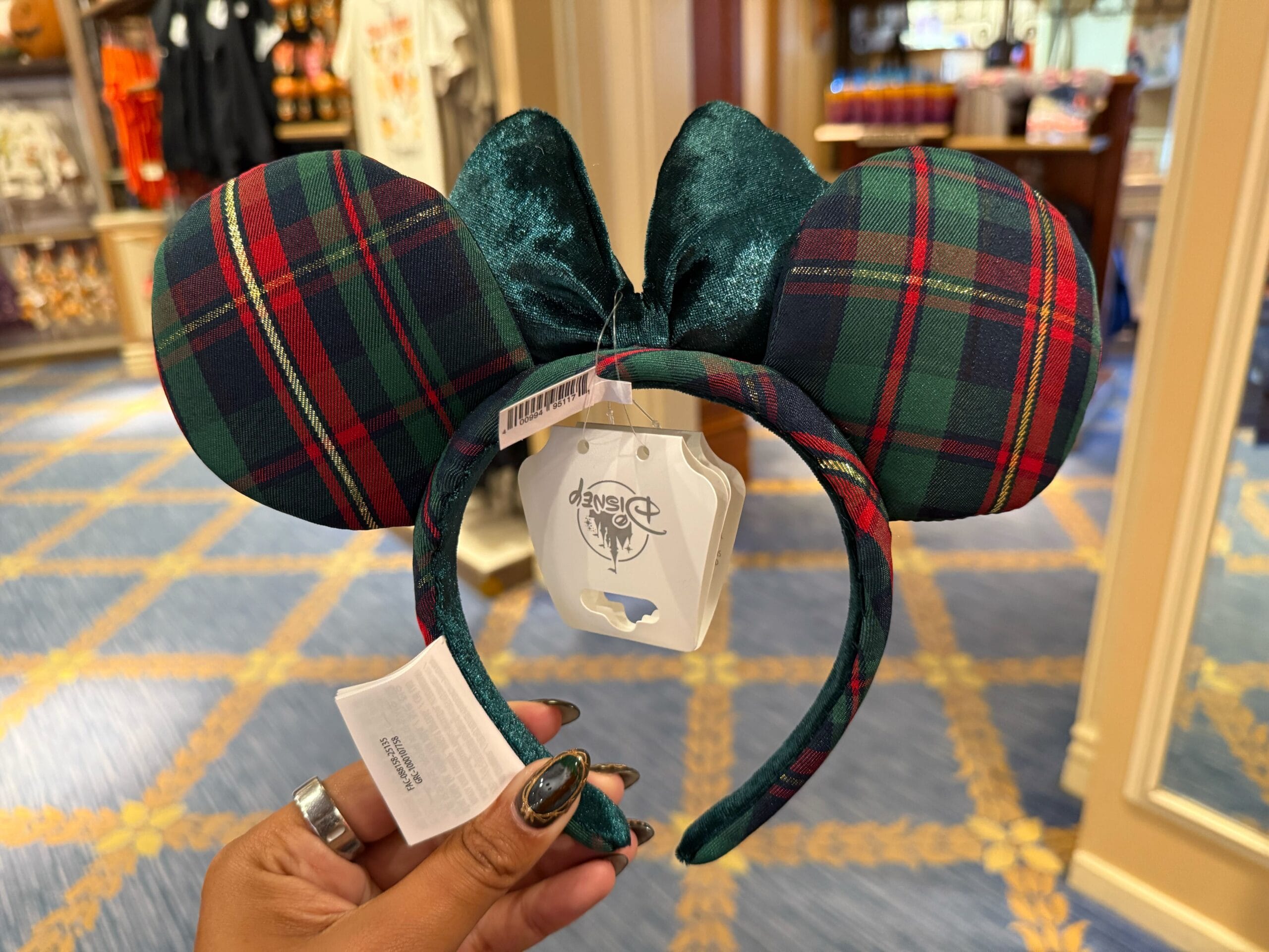 A hand holds plaid Mickey Mouse ears headband with a green velvet bow—festive 2025 Disneyland Christmas merchandise in store.