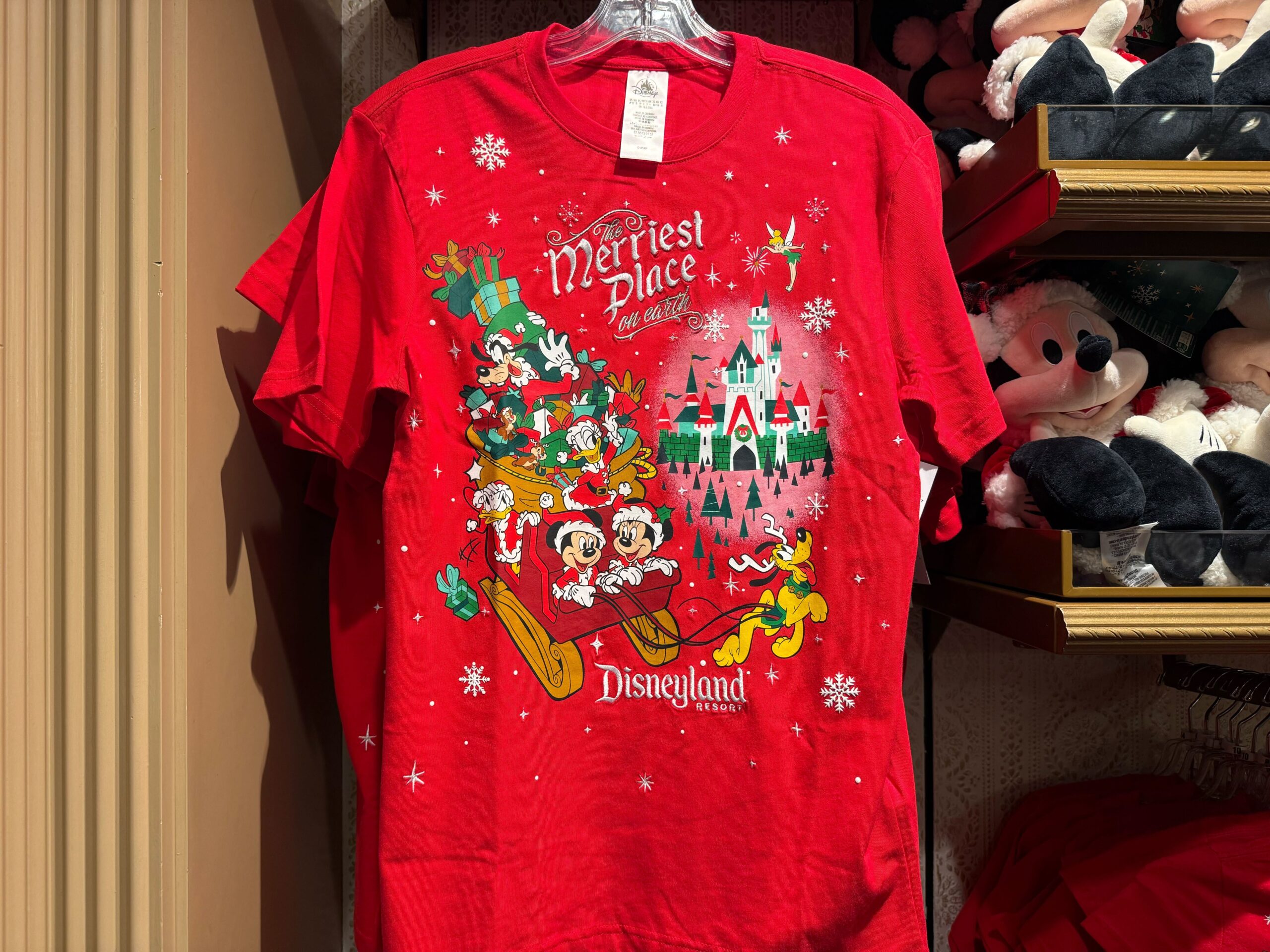 Red Disneyland Christmas merchandise shirt with Mickey & friends in a sleigh, snowy castle, and "Merriest Place" 2025 text.