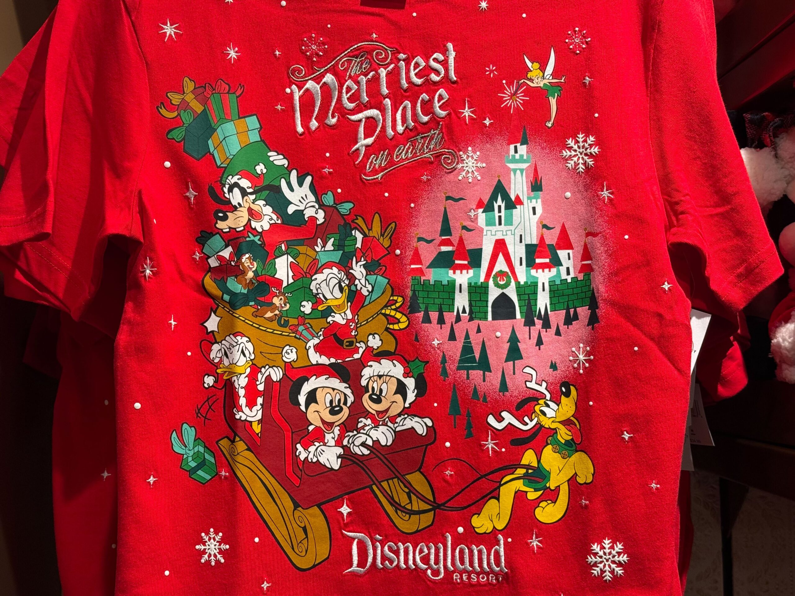 Red Disneyland Christmas Merchandise shirt featuring Mickey, Minnie, Goofy, and Pluto on a sleigh with castle, 2025 design.