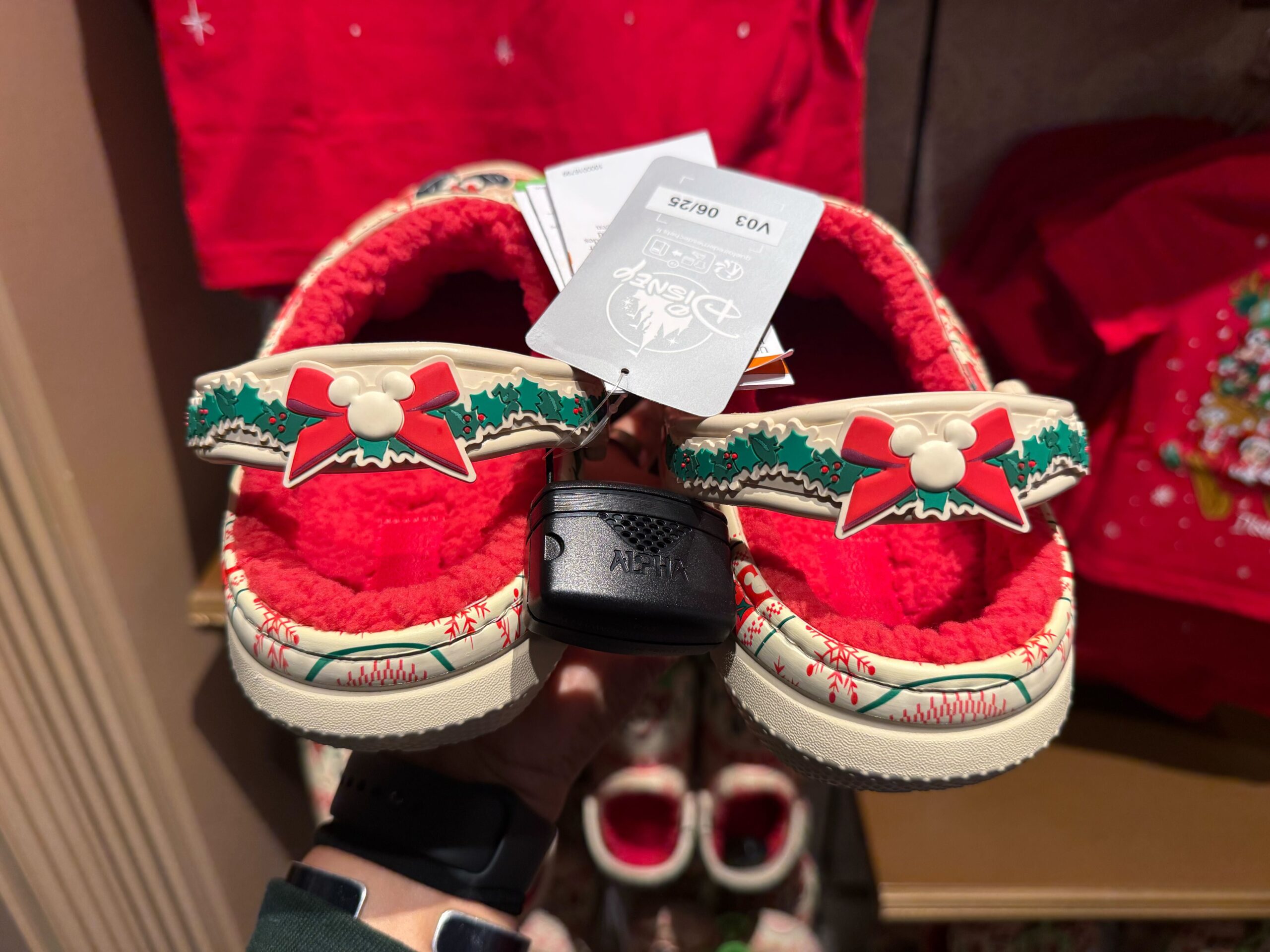 A pair of festive red and cream fuzzy clogs from Disneyland Christmas Merchandise 2025, held up in a store.