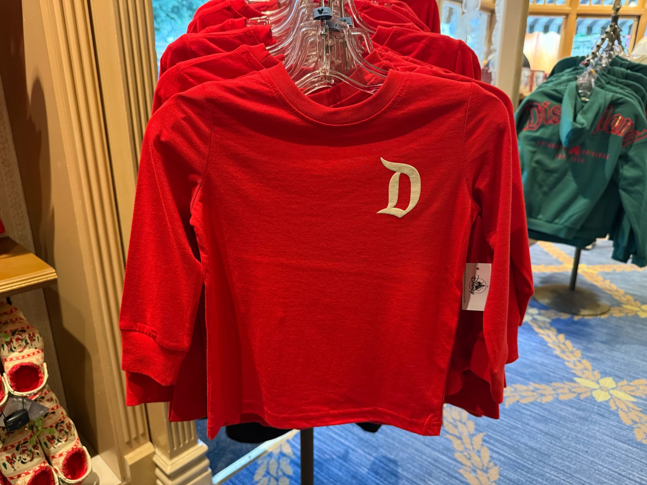 A red long-sleeve shirt with a white "D" on the chest—part of the 2025 Disneyland Christmas merchandise collection.