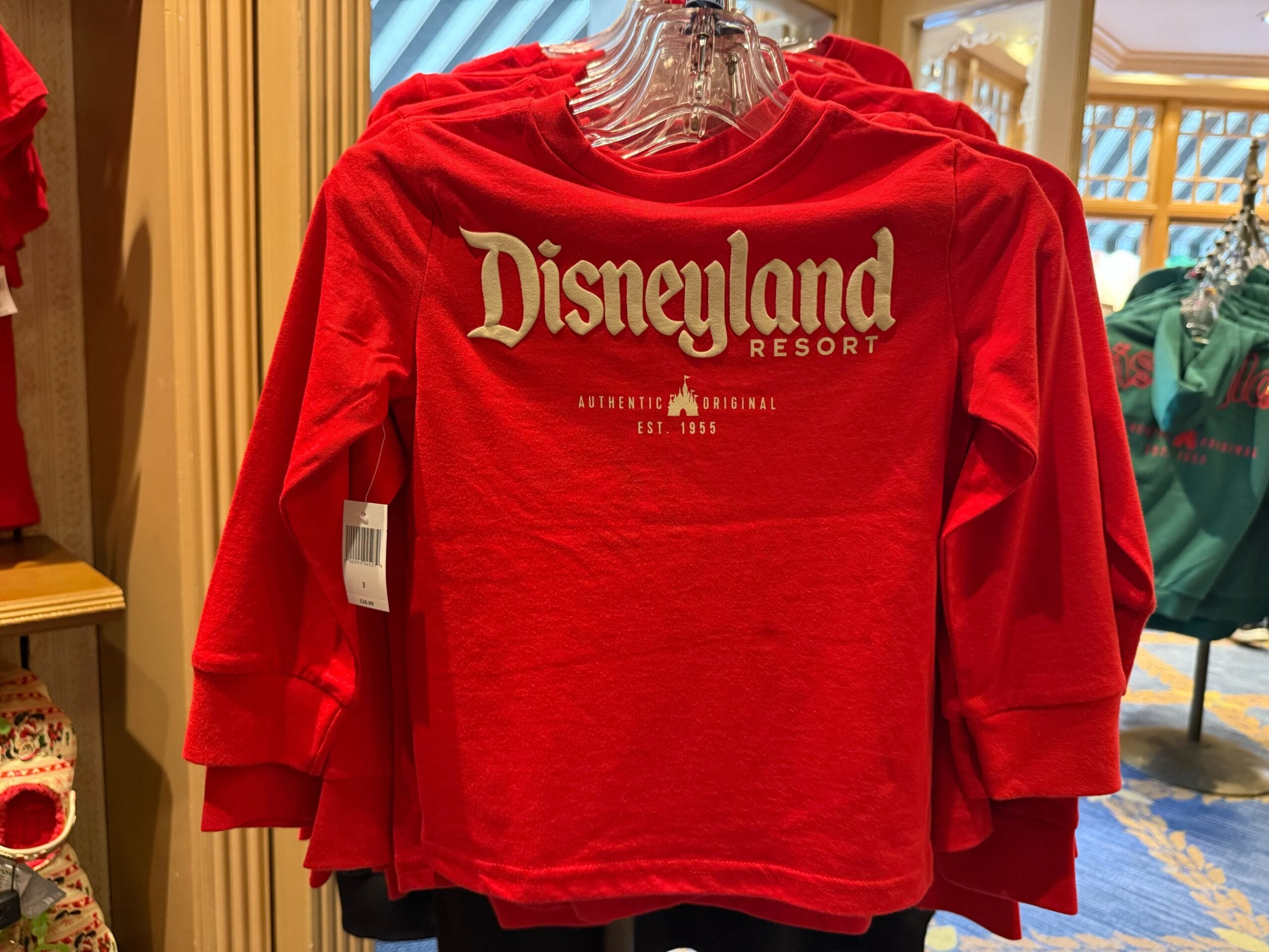 Red long-sleeve shirt with "Disneyland Resort" logo featured among 2025 Disneyland Christmas merchandise on a store rack.