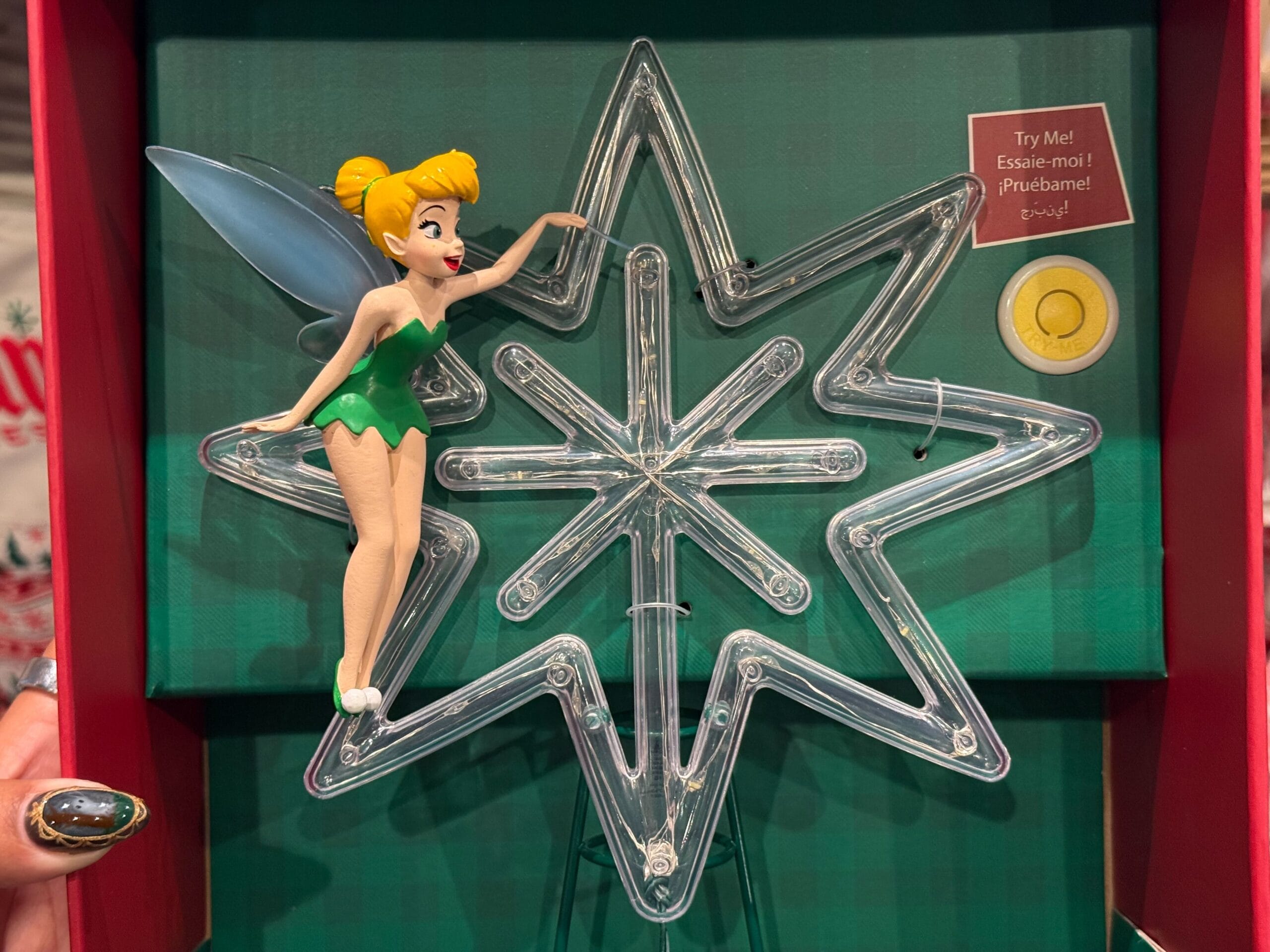 A Tinker Bell figurine stands on a light-up star, part of the 2025 Disneyland Christmas merchandise display box.