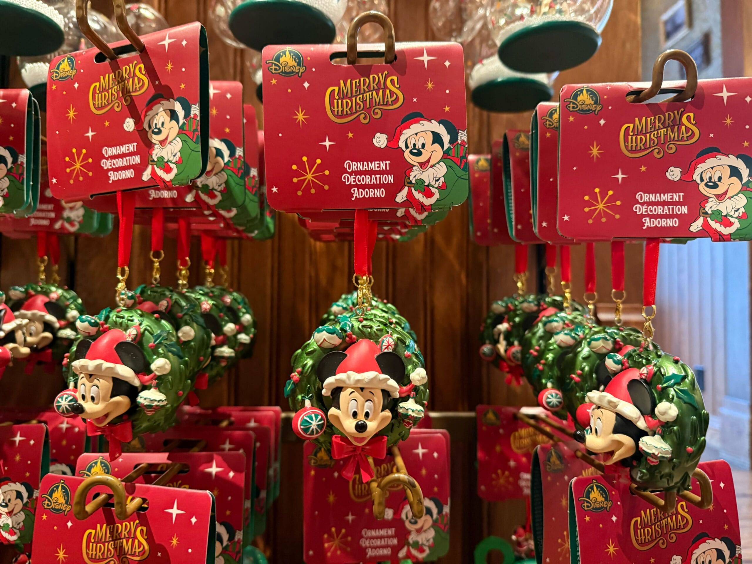 Mickey Mouse Christmas ornaments with wreaths from the 2025 Disneyland Christmas merchandise hang on display in a store.