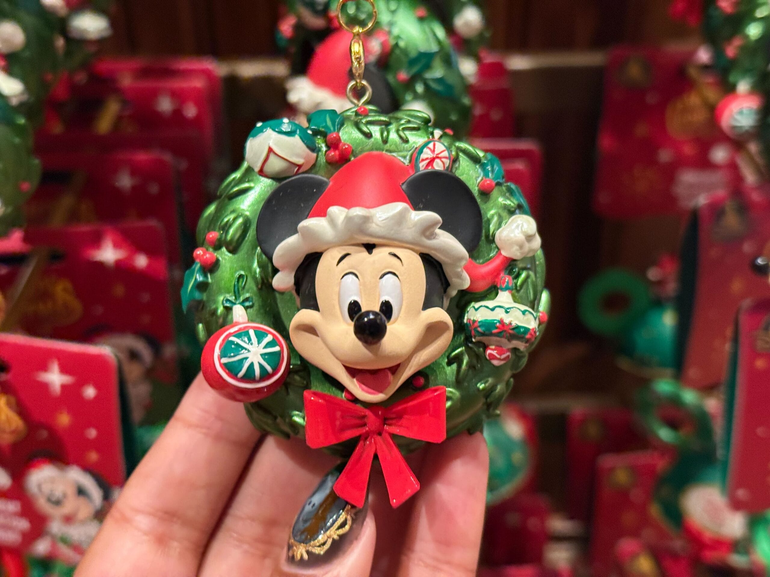 A hand holds a Disneyland Christmas Merchandise 2025 Mickey Mouse wreath ornament with Santa hat and festive decorations.