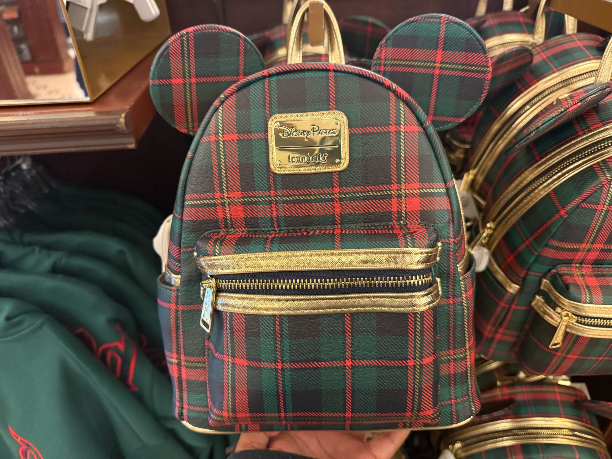 Plaid Christmas Loungefly Mini Backpack with Mickey Mouse ears and gold zippers, in a Disney Park store, no castle visible.