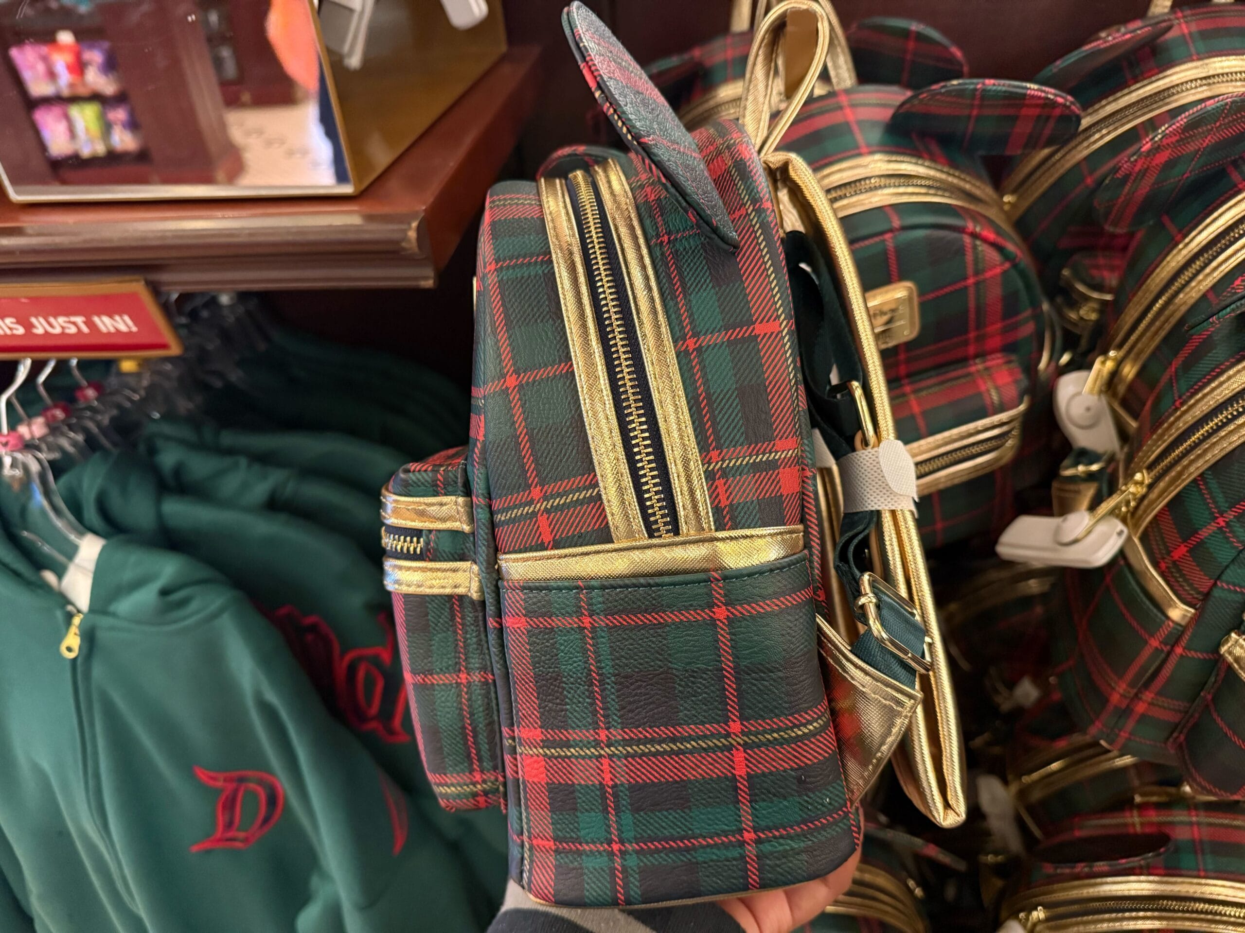 A hand holds a Plaid Christmas Loungefly mini backpack with gold zippers among similar holiday bags at a Disney Parks gift shop.