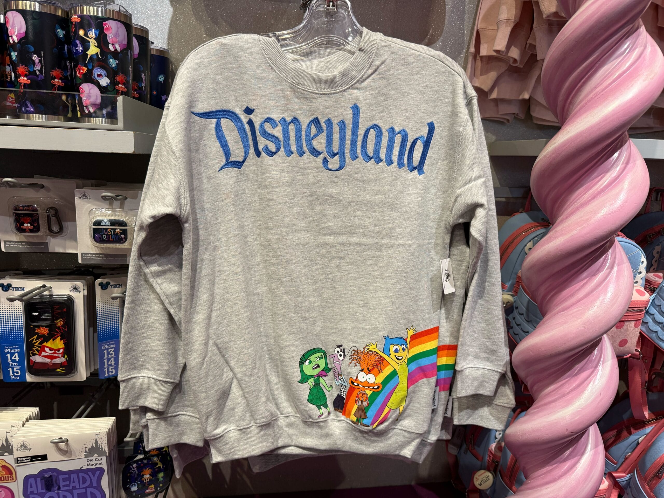 Gray Disneyland sweatshirt featuring Pixar characters and a rainbow, displayed among other park merchandise