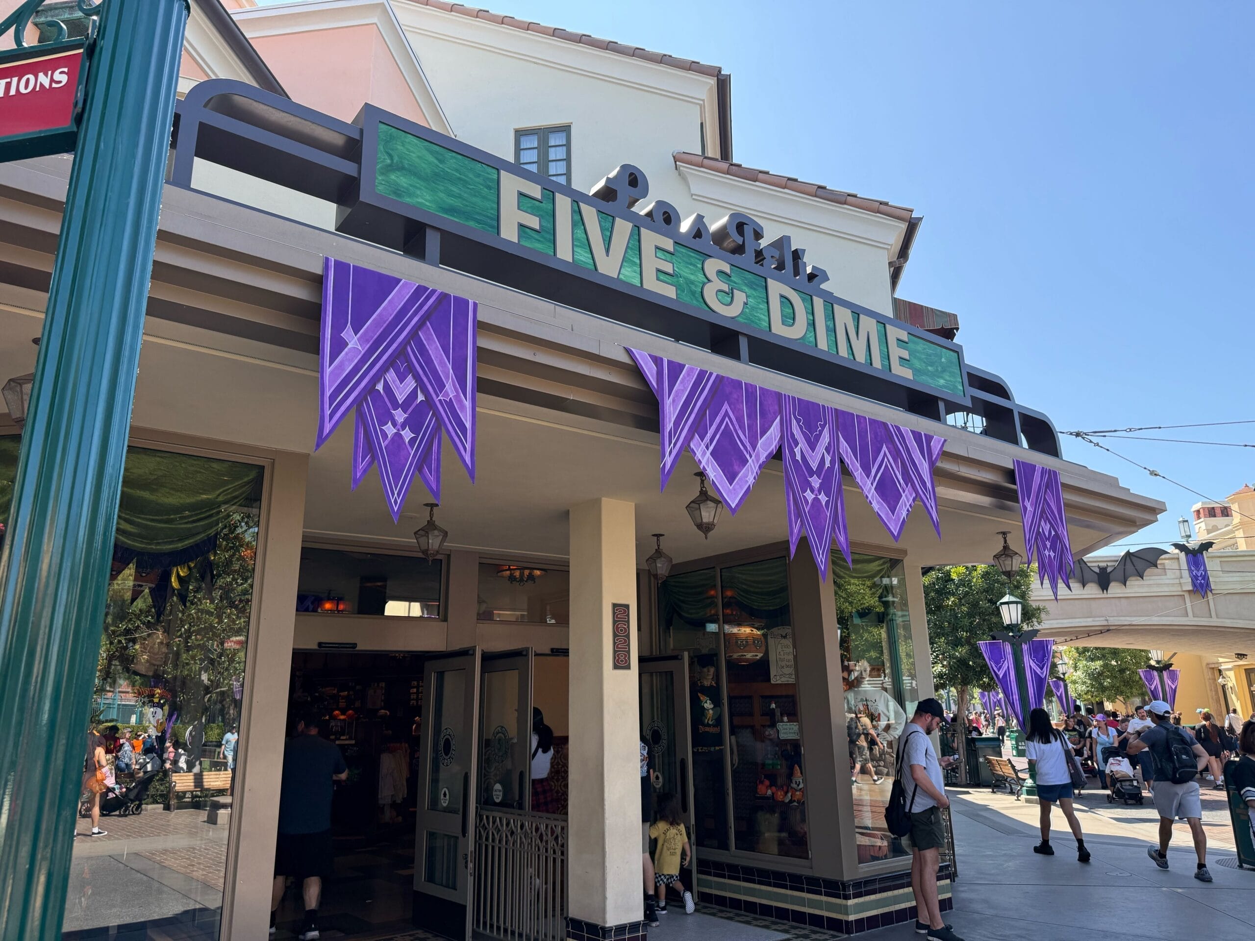 Guests stroll past Disneyland's Five & Dime store, adorned with Halloween themed purple banners, under clear skies near Main Street U.S.A.