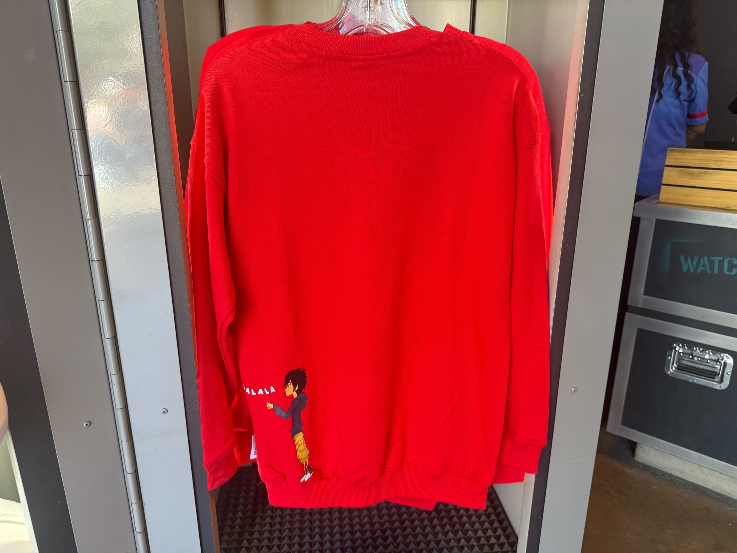 Red sweatshirt displayed in a park shop, featuring a small cartoon of Miles Morales near the hem