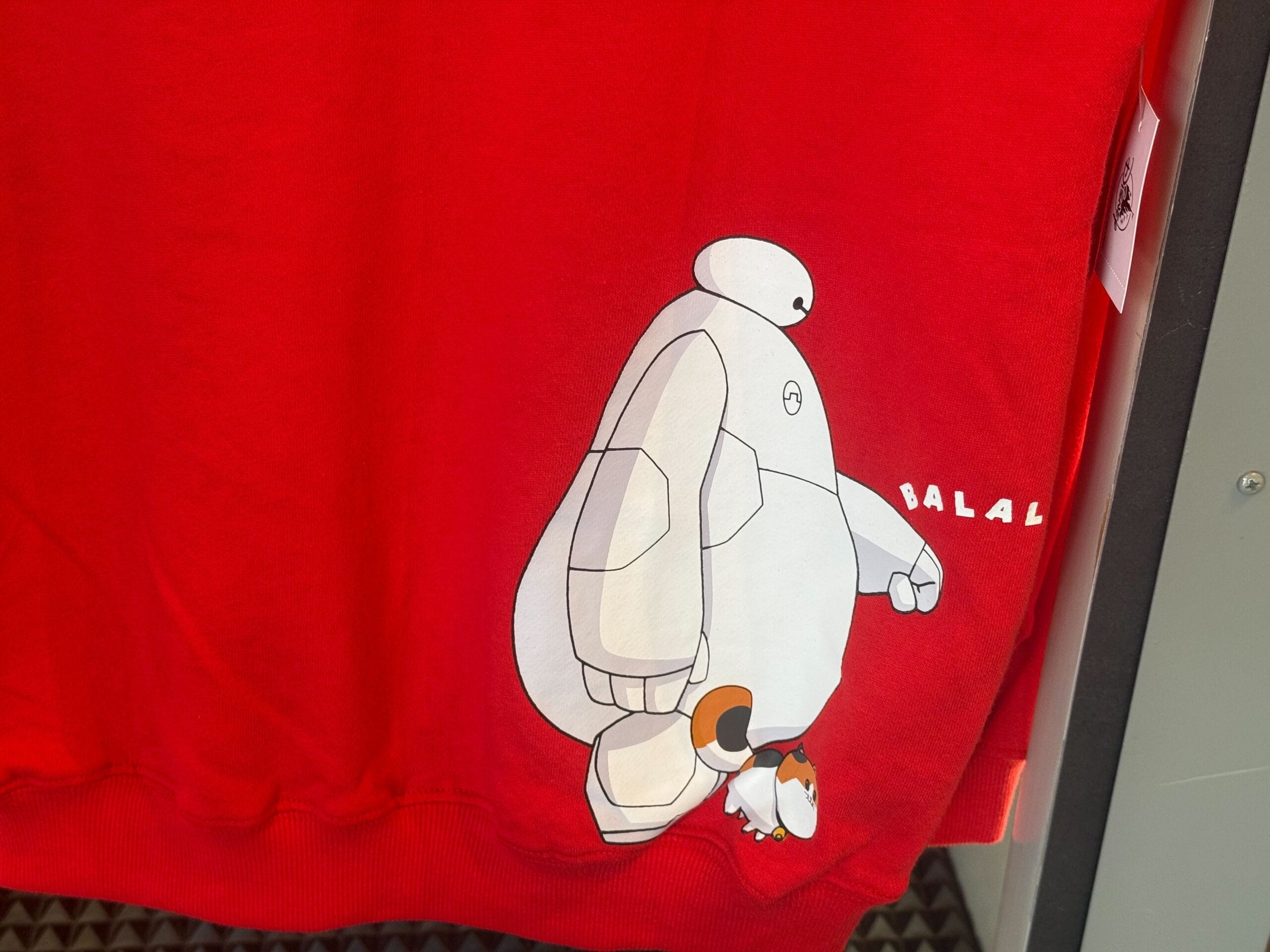 Red shirt with Baymax from "Big Hero 6," a small penguin, and "BALALALA"—a fun design you might spot at a Disney park shop.