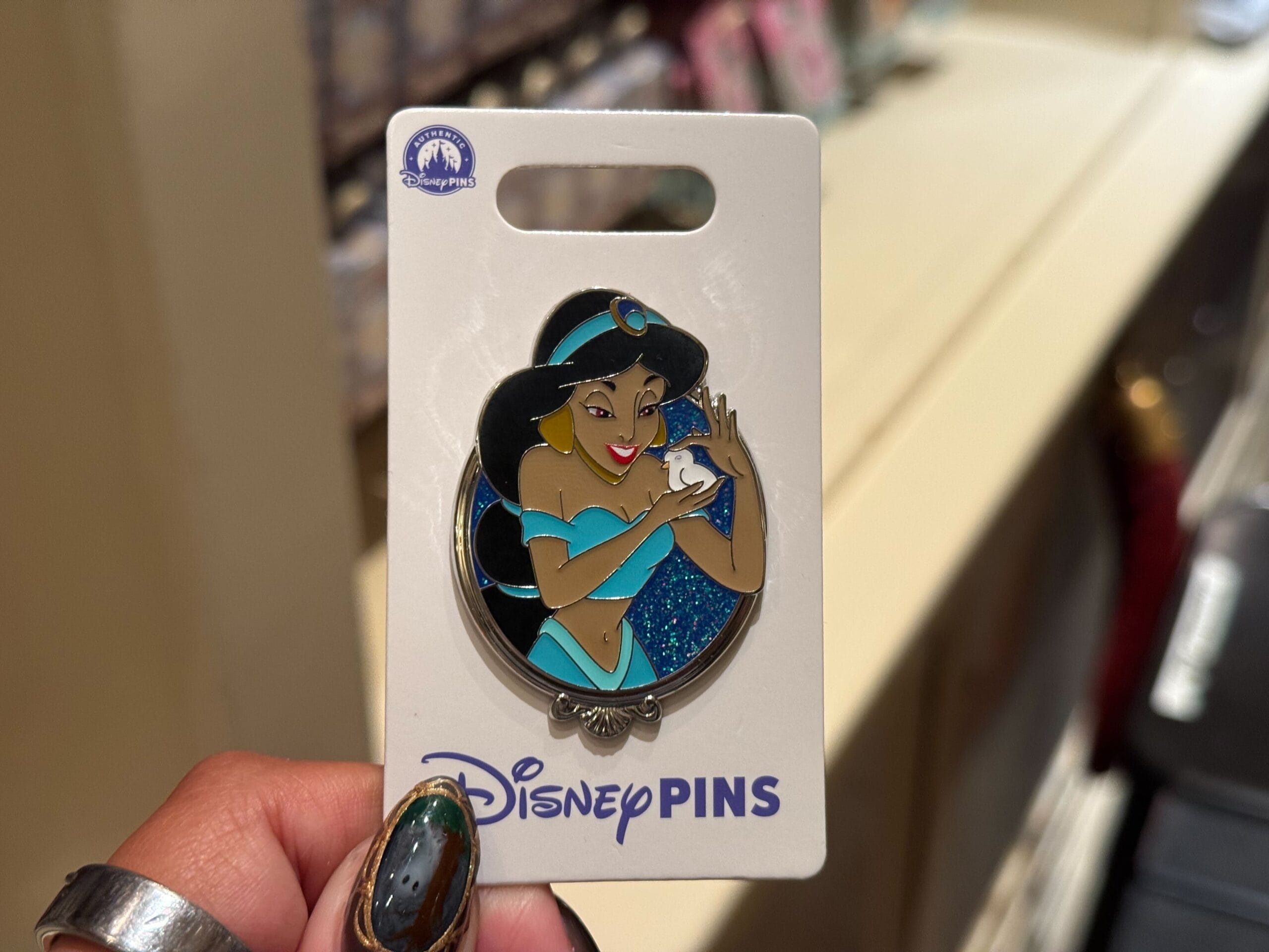 A hand displays a Disney Princess pin of Jasmine smiling, reminiscent of characters seen in Walt Disney World’s parks.