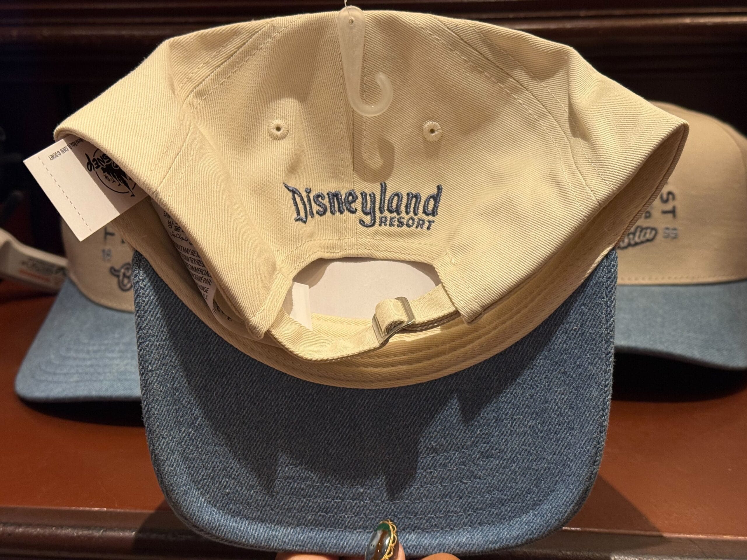 A beige and blue Disneyland Resort hat sits on a store shelf, its style unique to Disneyland compared to other Disney Parks.
