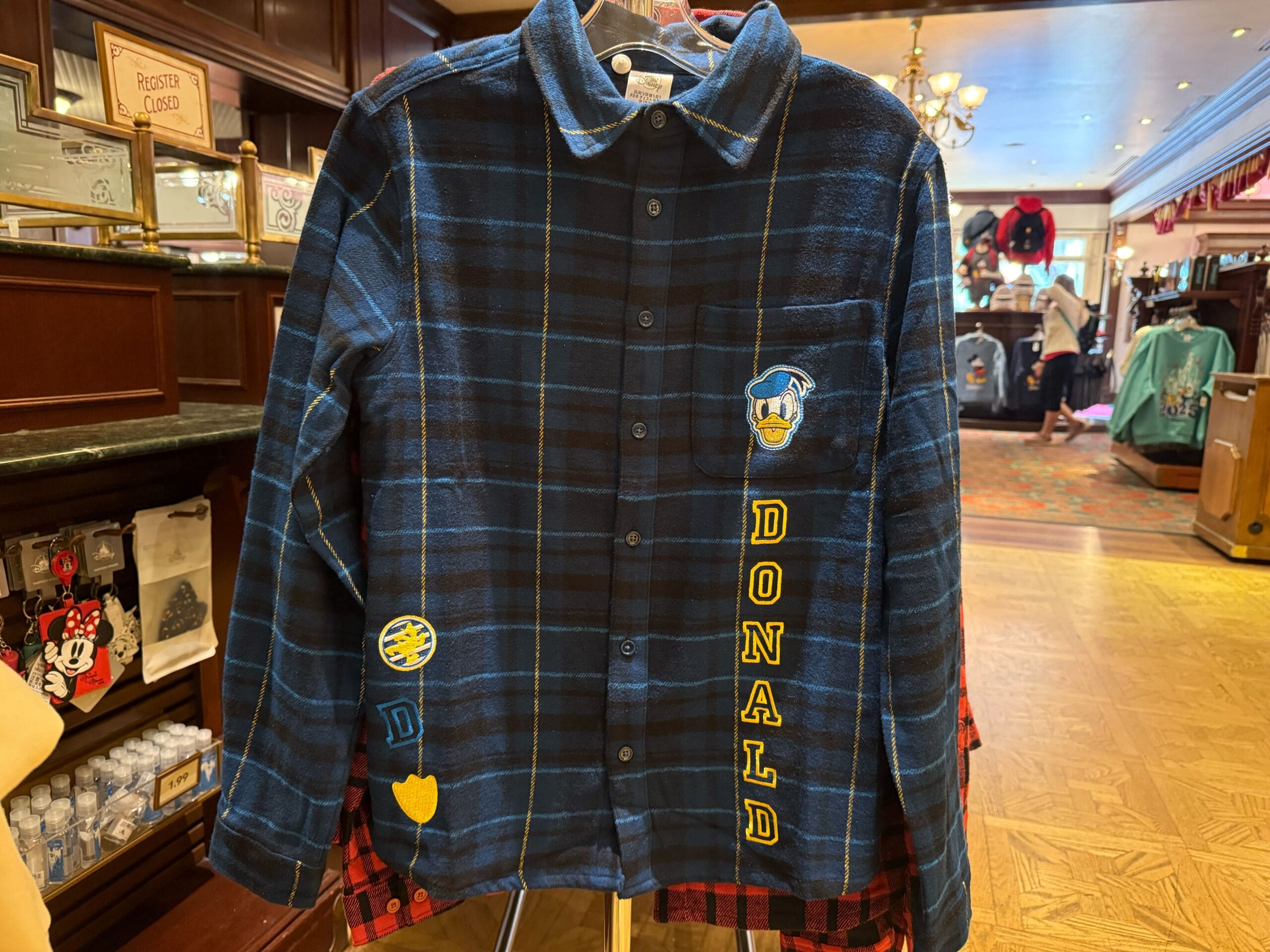 Blue plaid flannel shirt with "DONALD" and Donald Duck patches, found among Disneyland merchandise near Sleeping Beauty Castle.