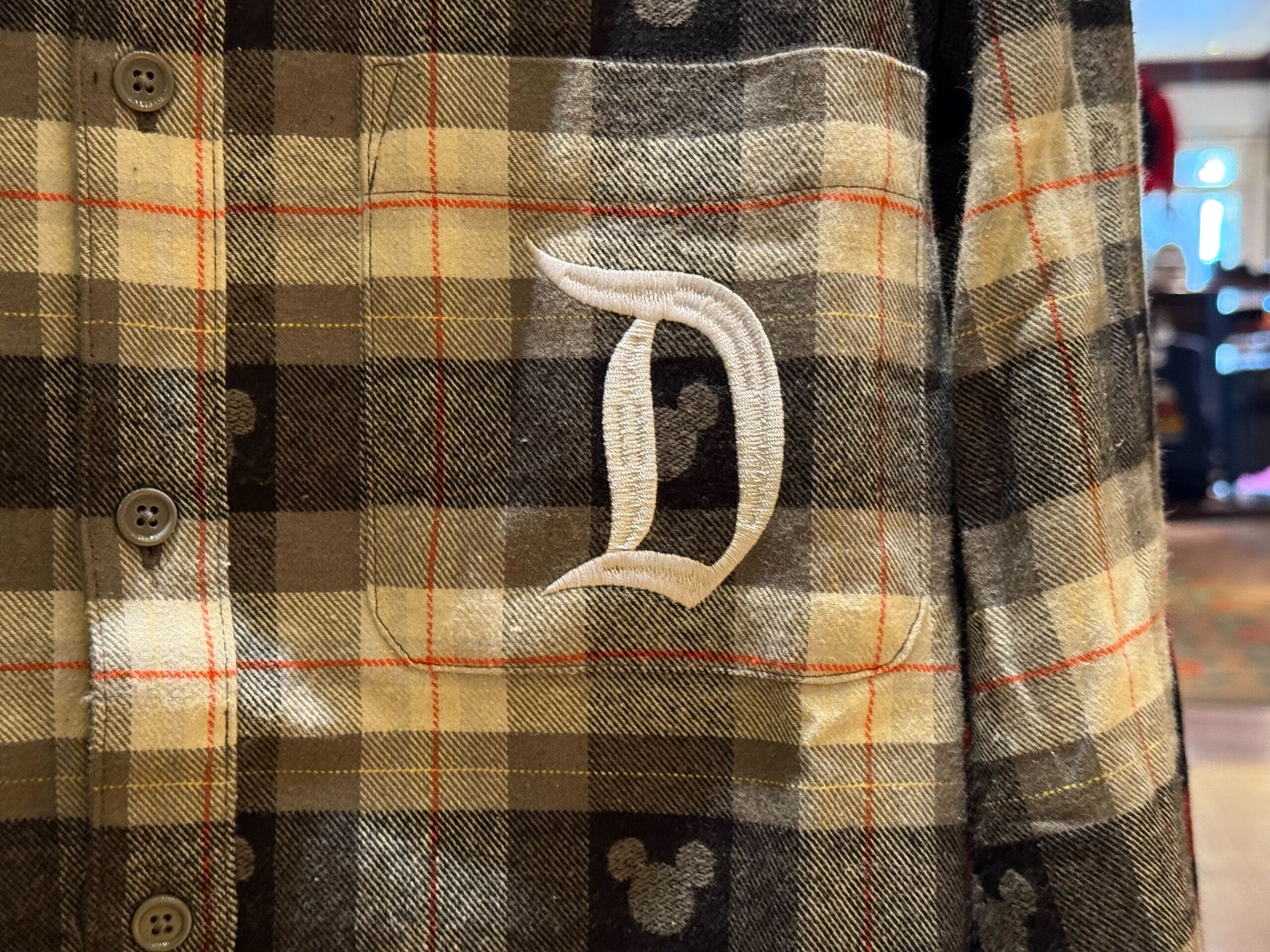 Plaid shirt featuring a white "D" embroidered on the chest pocket—classic Disneyland merch, echoing signature park style.