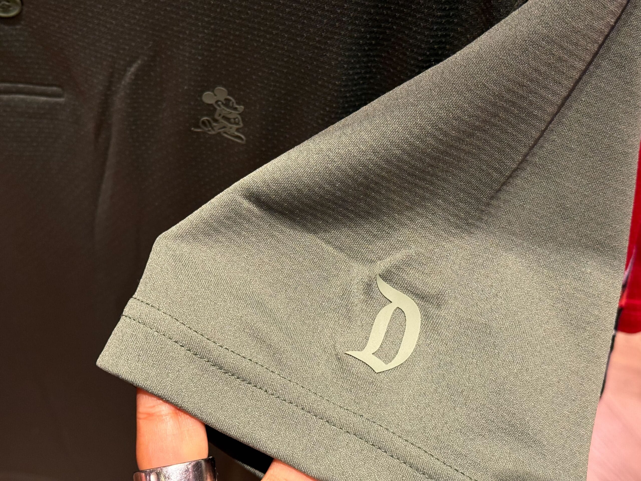 Close-up of a shirt sleeve with “D” logo and small Mickey Mouse on chest—iconic Disneyland merch, reminiscent of Main Street style.