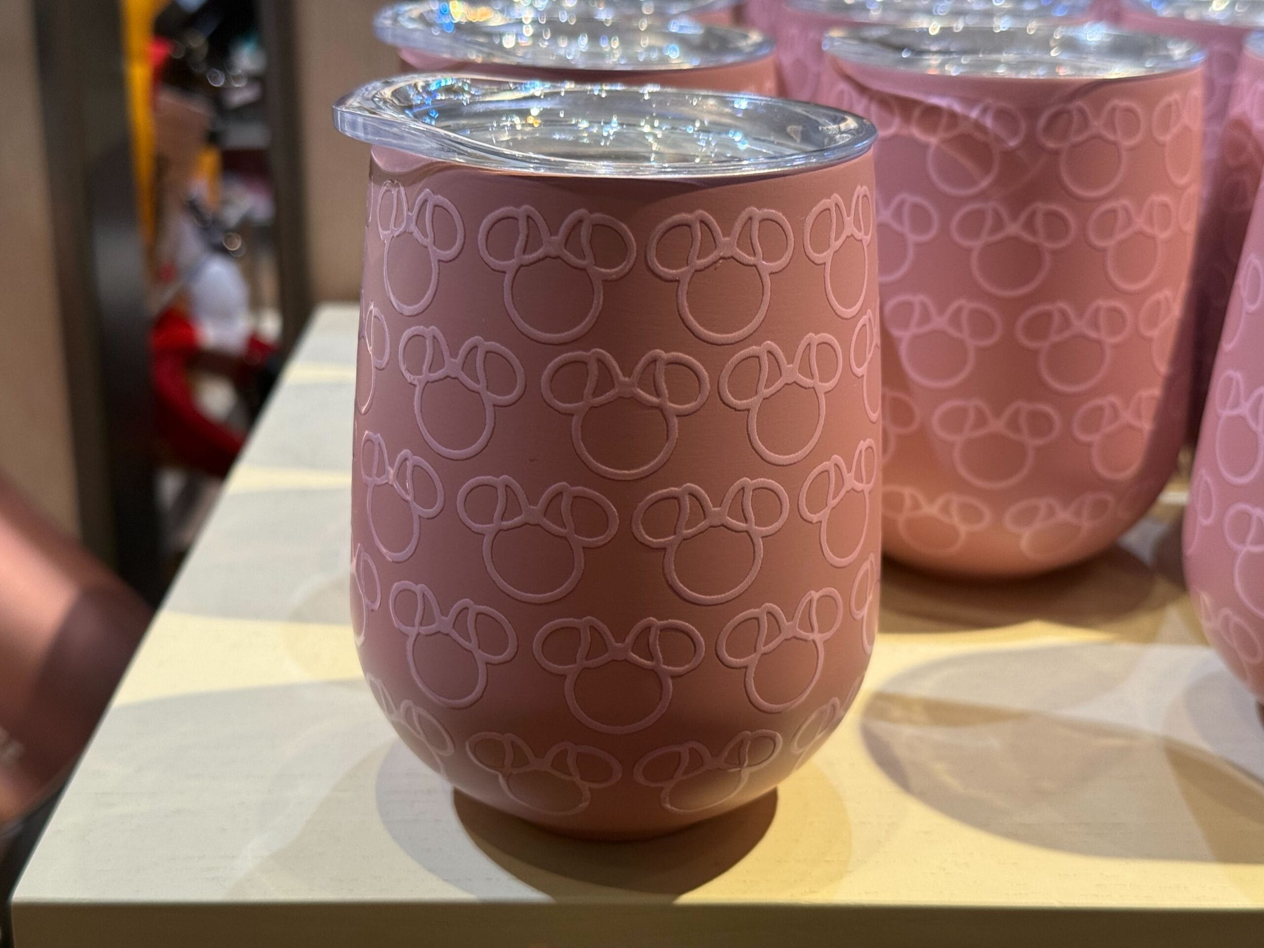 Pink Disney Parks tumbler with a clear lid, featuring repeating outlines of classic Mickey Mouse heads in a playful pattern.