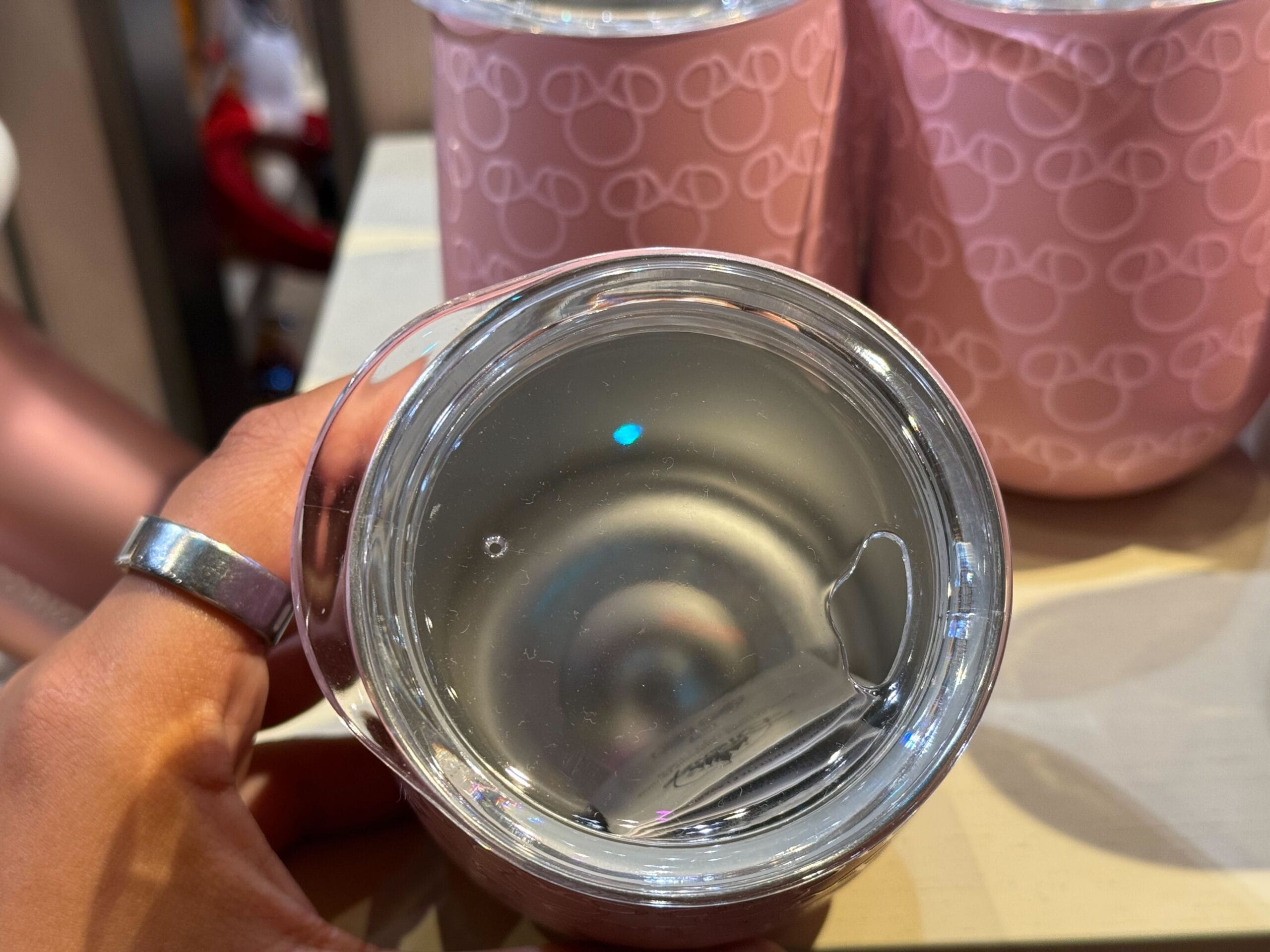 Hand holding a pink cup with clear liquid, surrounded by more pink Mickey Mouse cups—classic Disney Parks snack vibes.