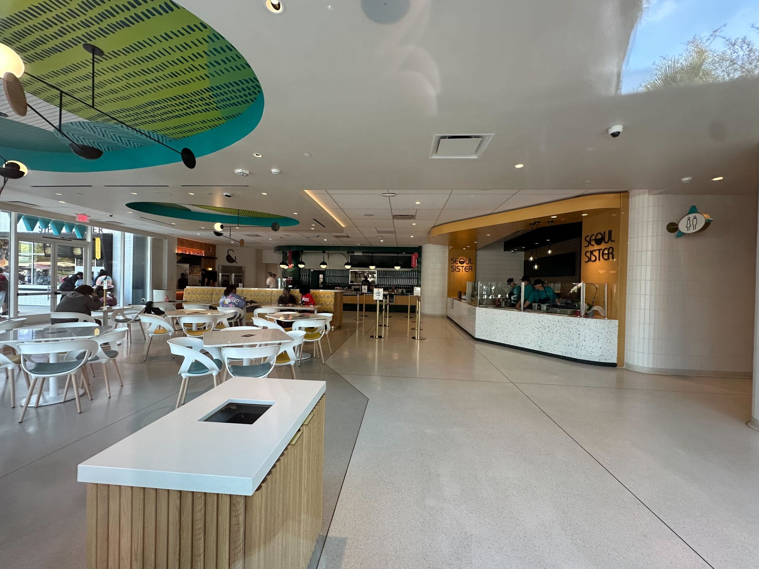 Modern Downtown Disney food court with white tables, chairs, and waste station by the closed Sip & Sonder counter—no castle in view.