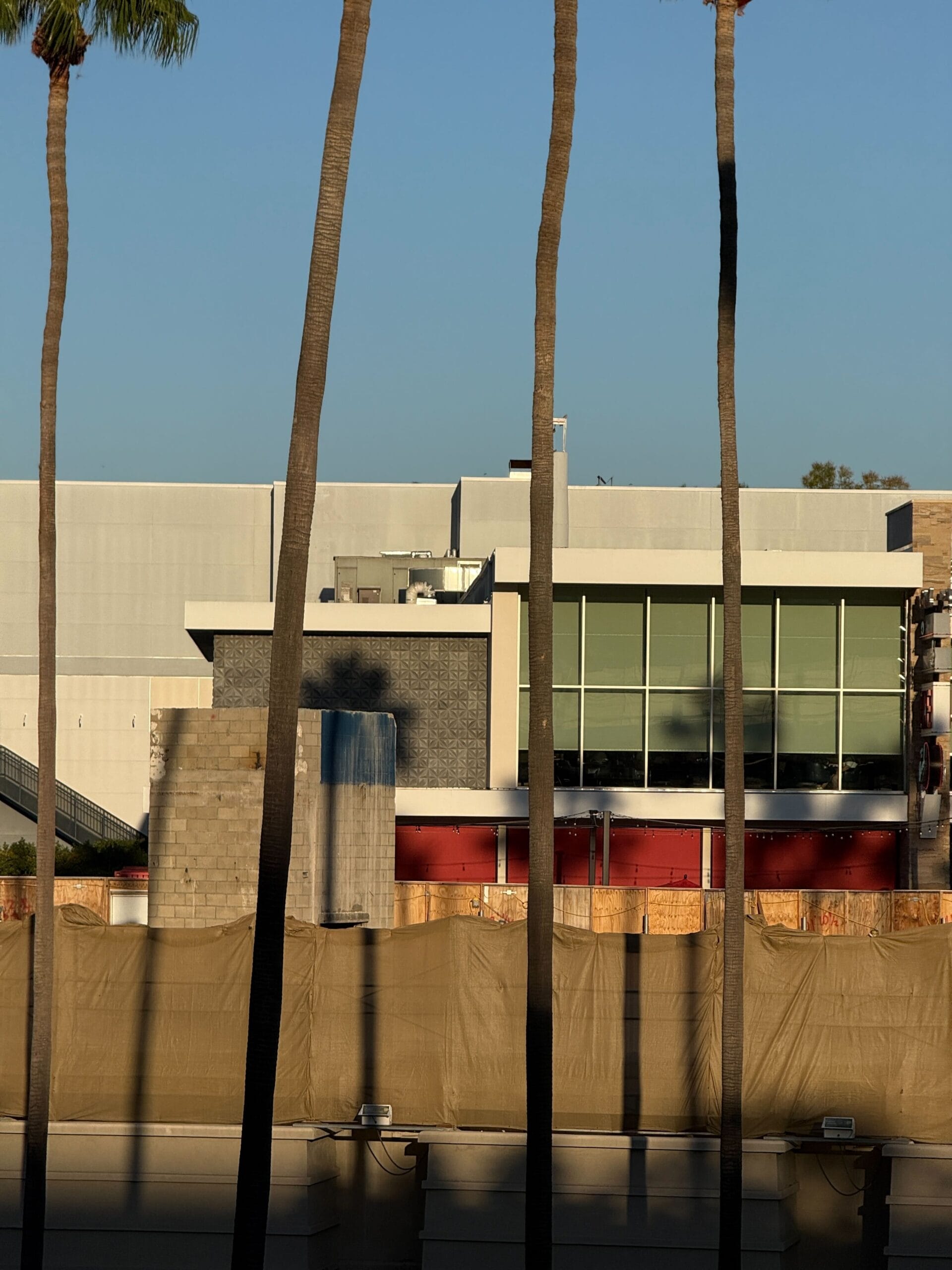 Contemporary building with expansive windows, palm trees, and tan construction fencing near Downtown Disney, no castle in view.
