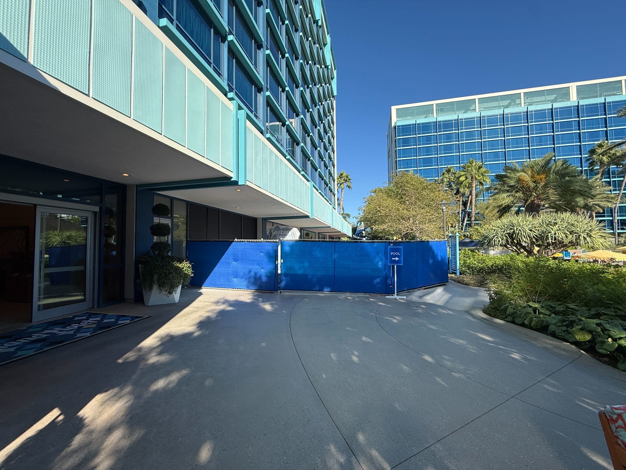 A blue Disneyland Hotel with a blue construction fence near the lobby entrance under a clear sky.