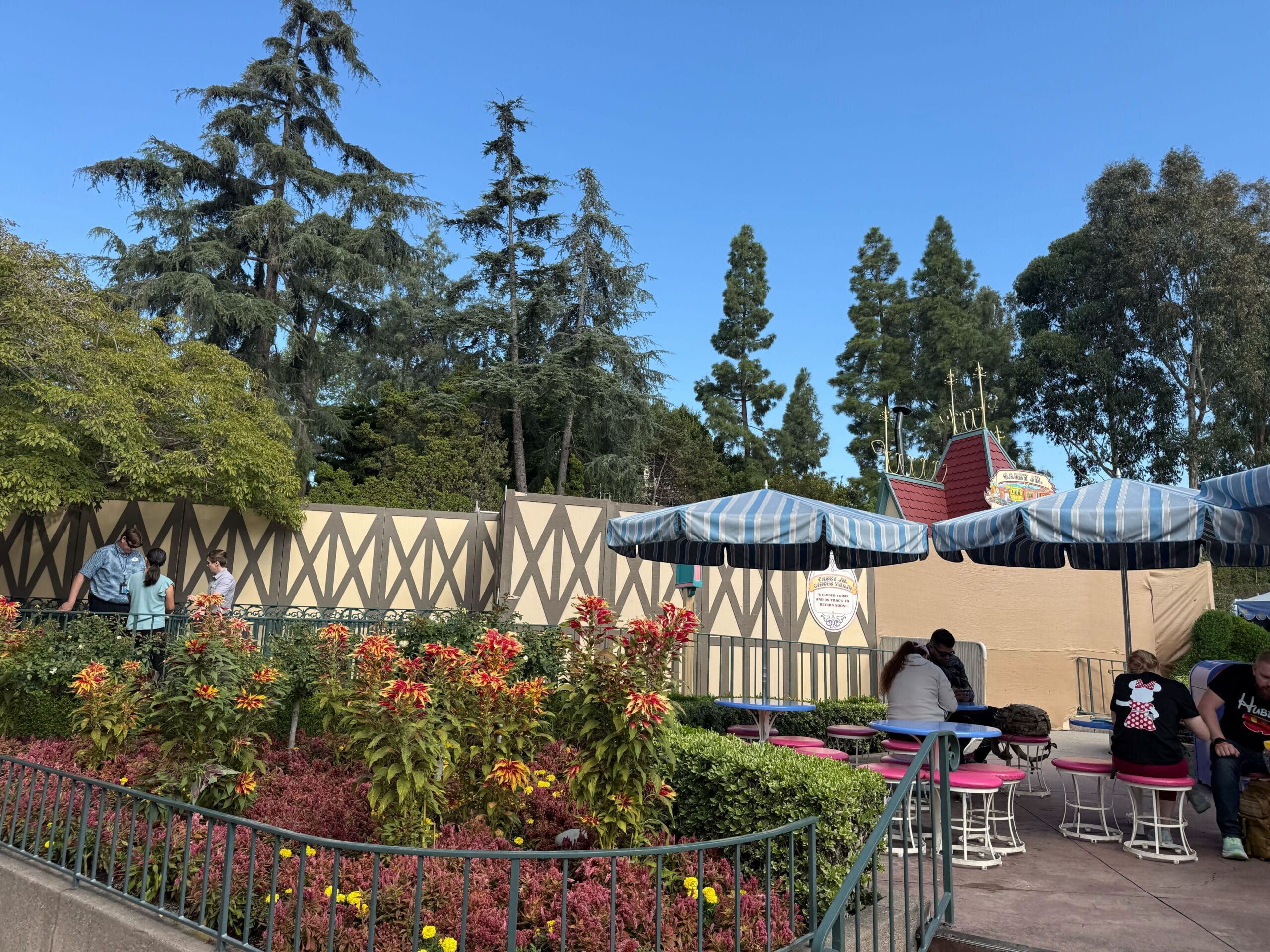 Outdoor seating with blue-striped umbrellas near construction walls at Disneyland, close to Casey Jr. Circus Train